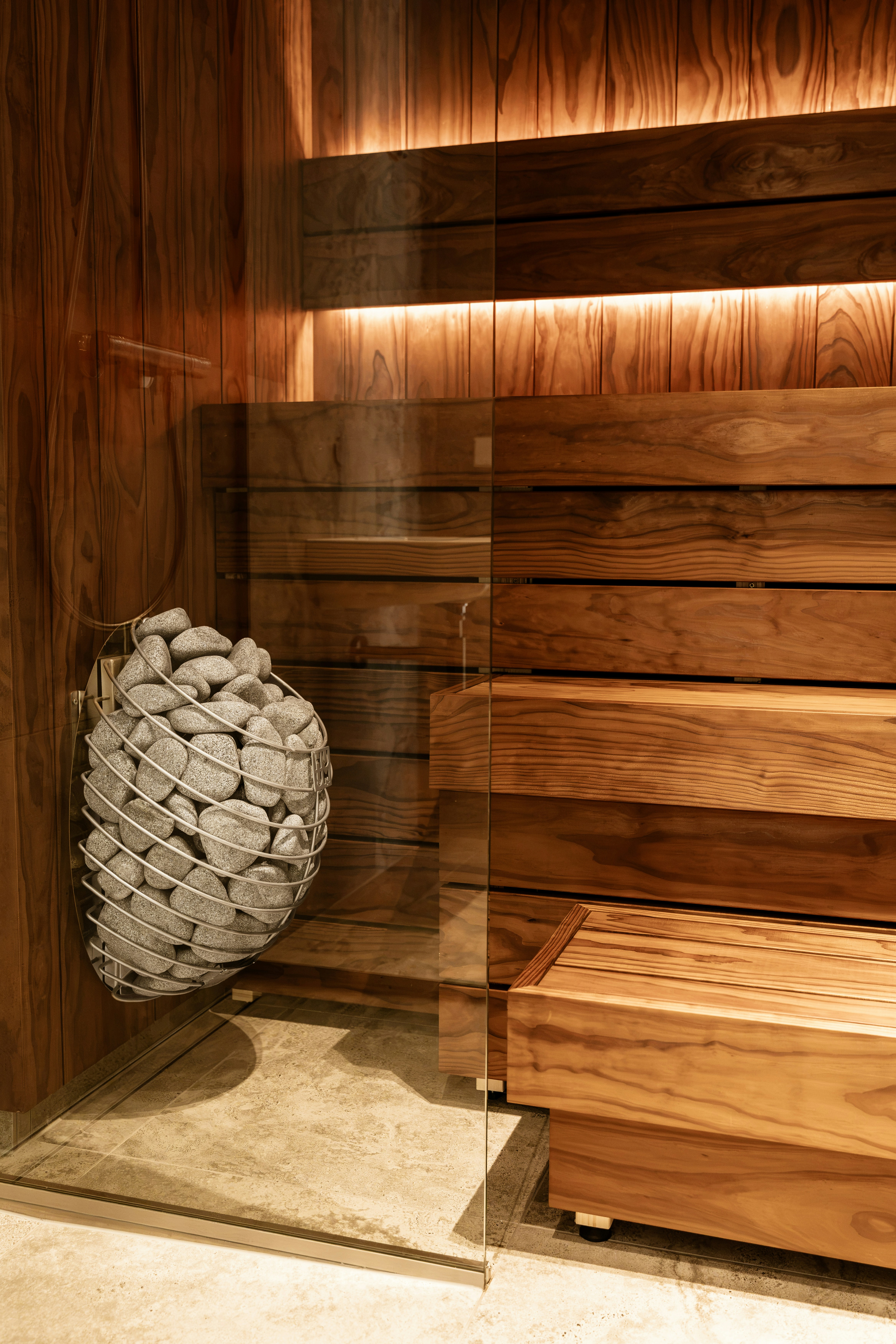 A wire basket filled with grey sauna stones beside wooden benches in a sauna