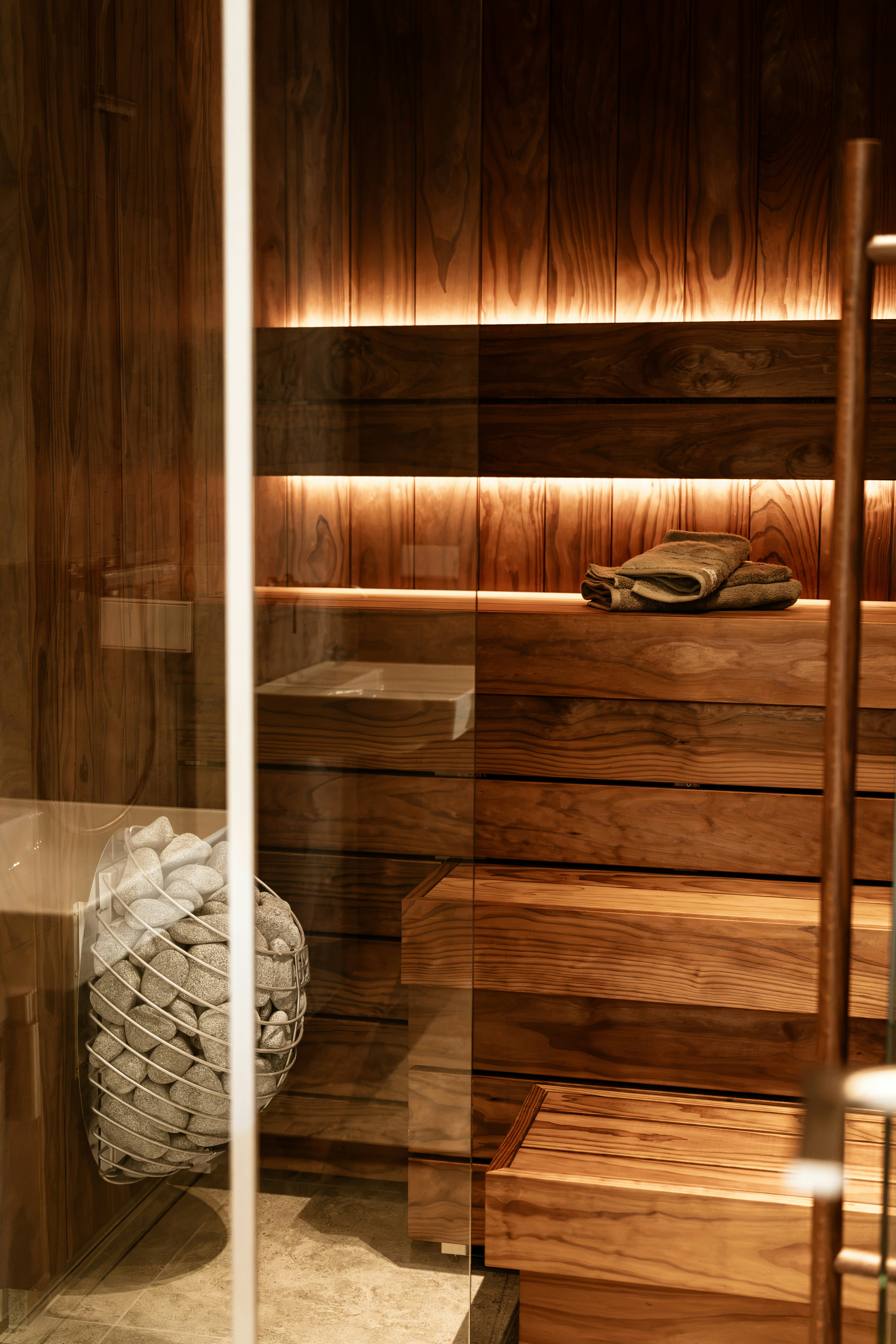 A sauna with wooden benches, a stone heater, and folded towels in a room