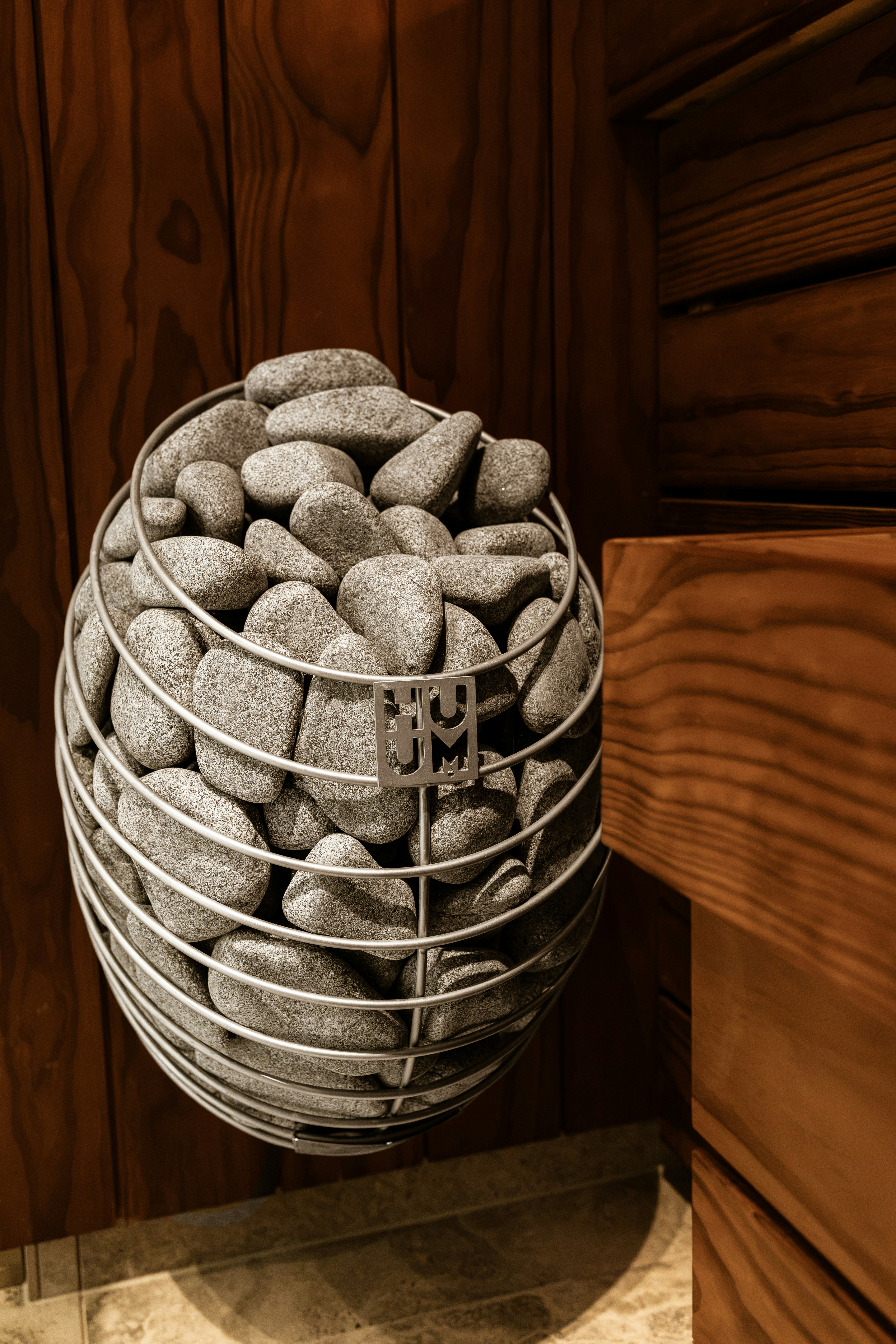 Grey sauna stones stacked inside a metal wire cage on a wooden wall