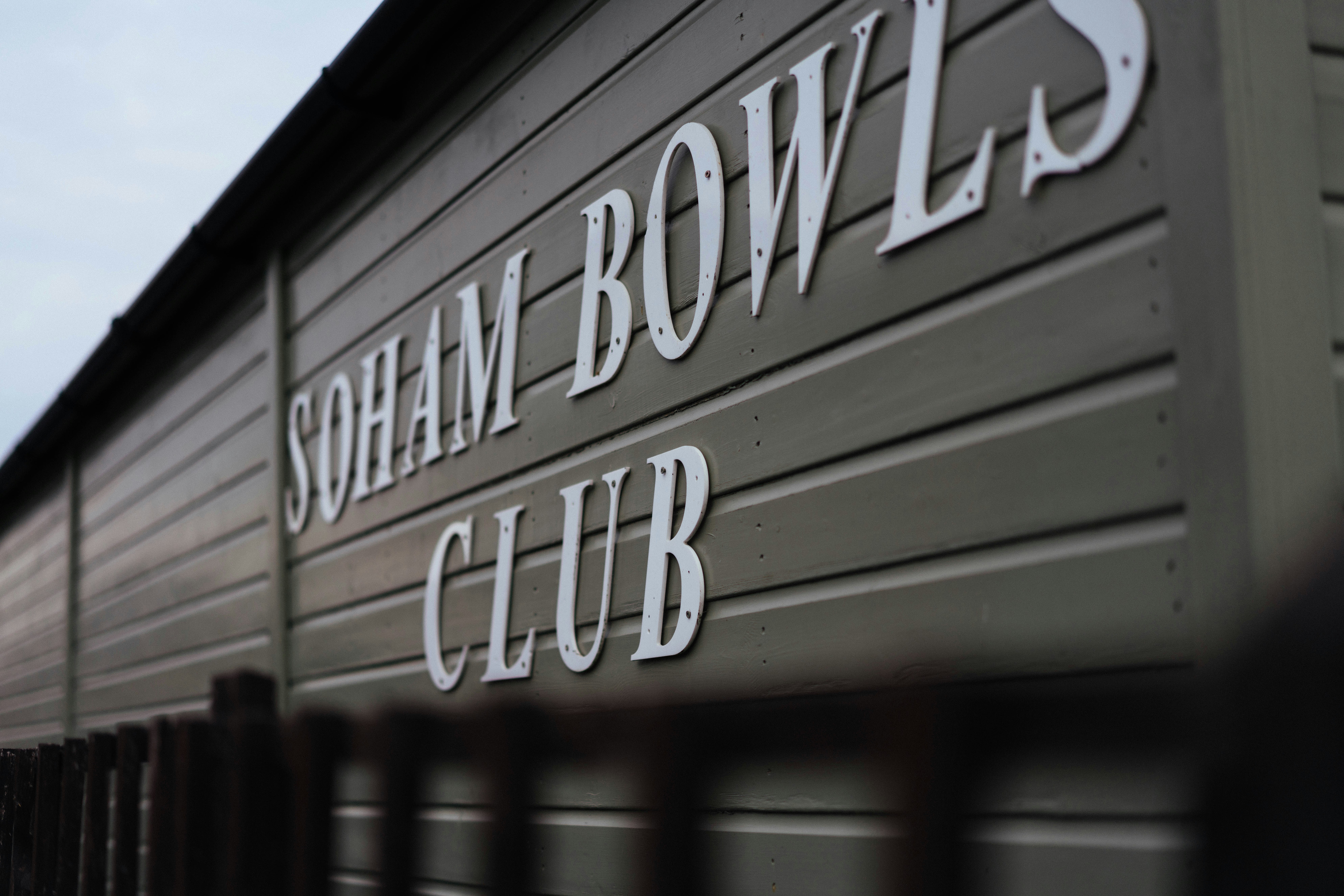 A sign reading Soham Bowls Club on the side of a grey building