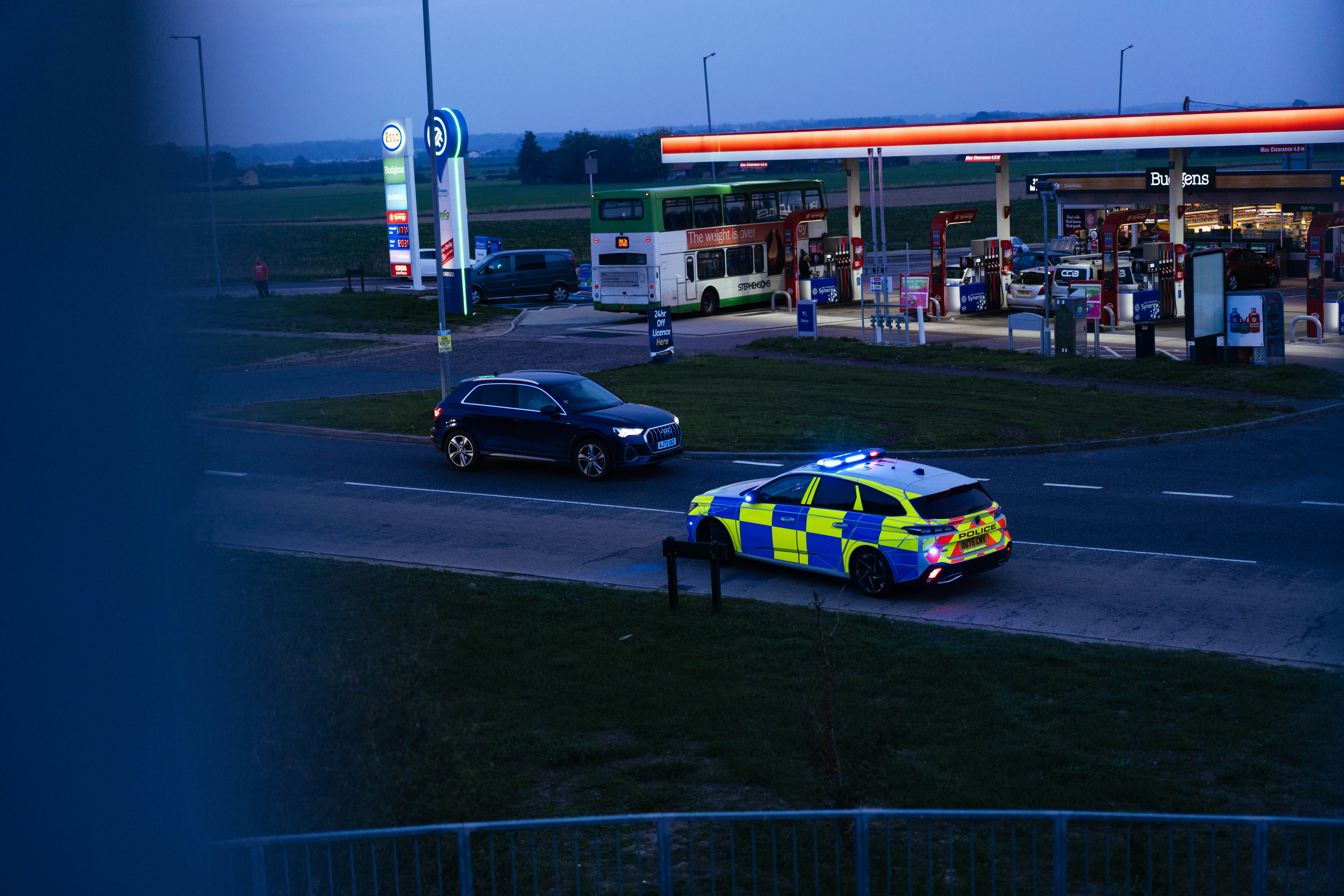 A police car with flashing blue lights near a gas station at dusk