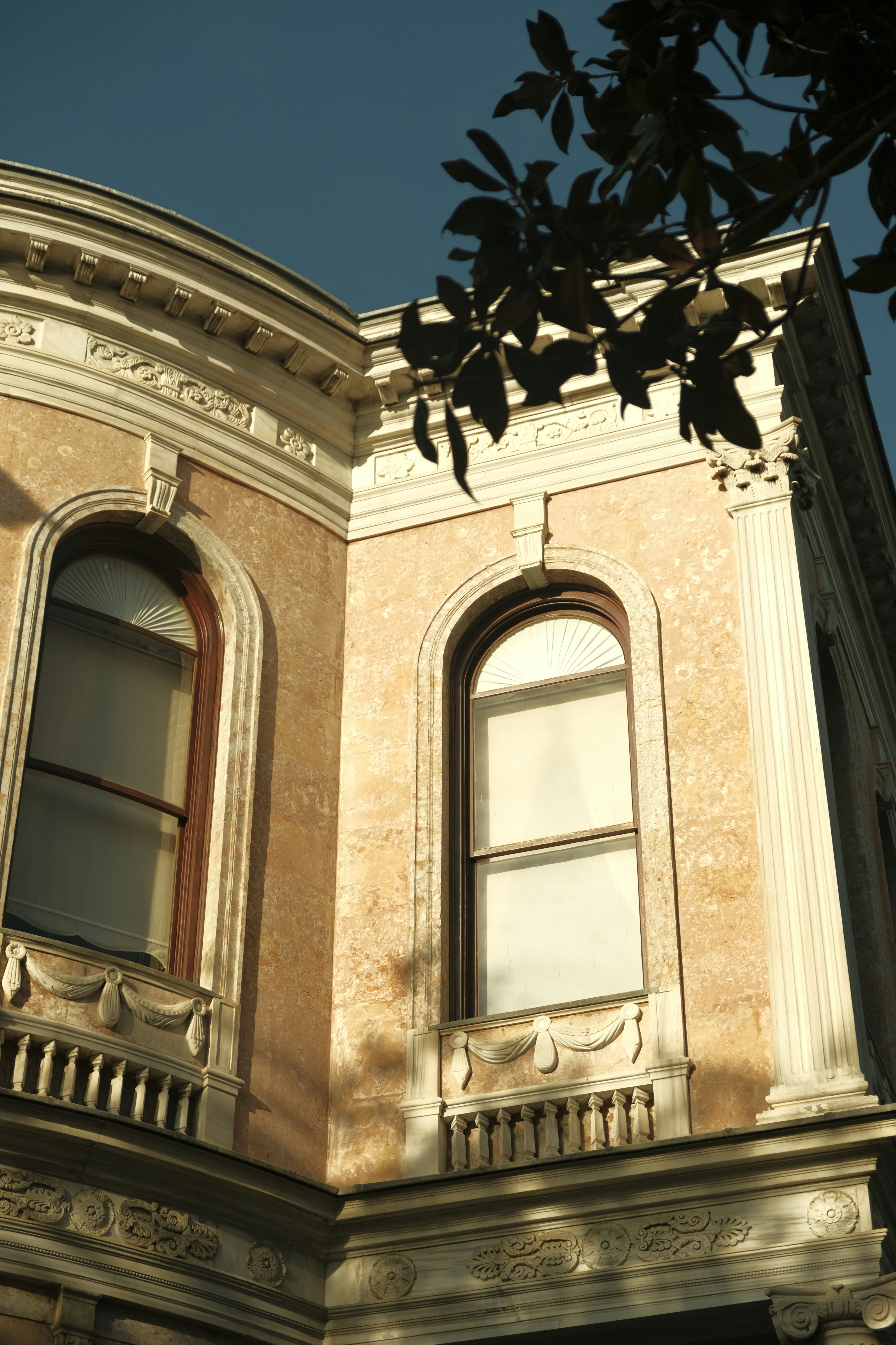 The corner of a neoclassical building with arched windows and ornate stone carvings