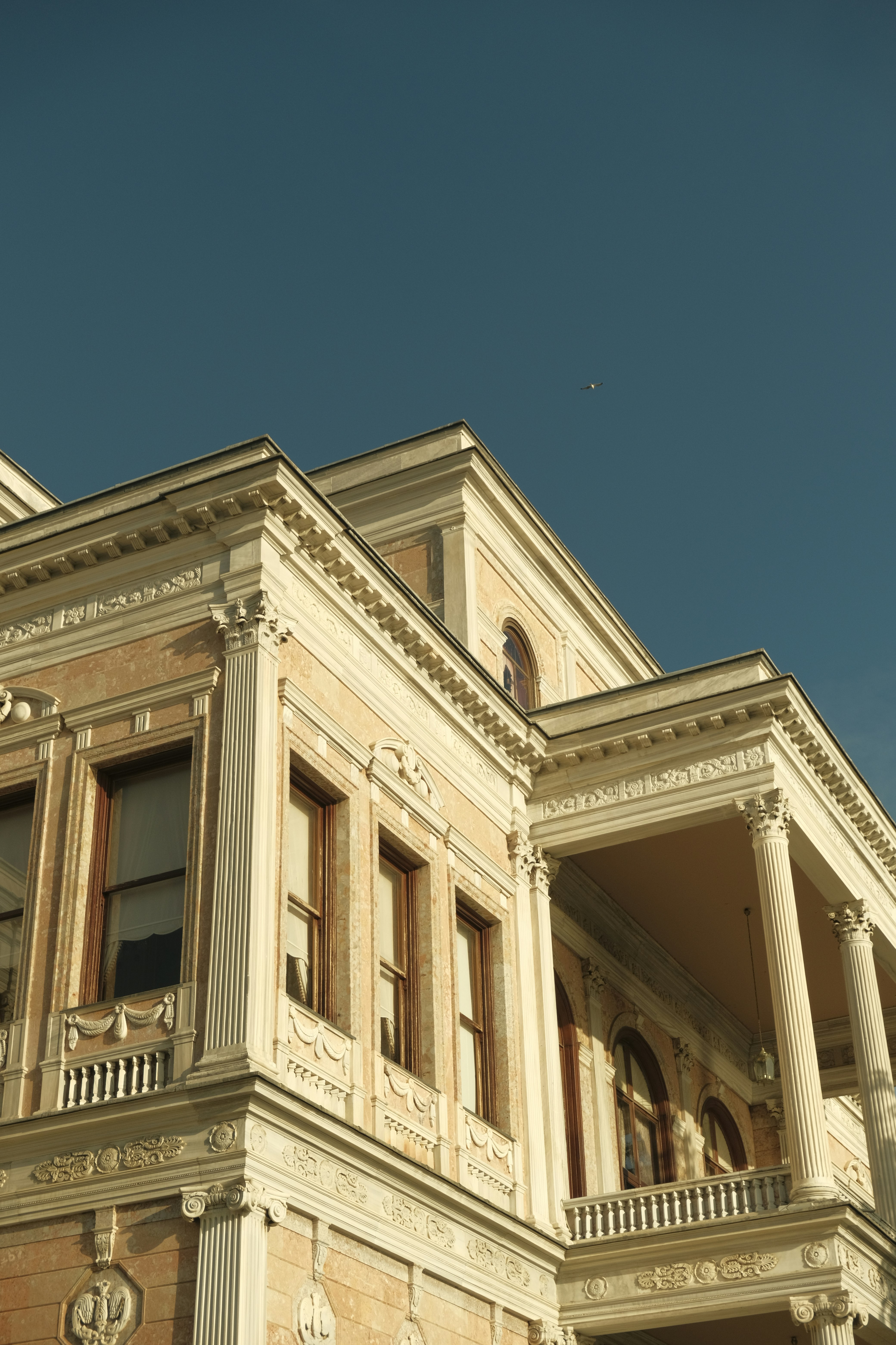 A neoclassical mansion with ornate columns and stone facade against a clear blue sky