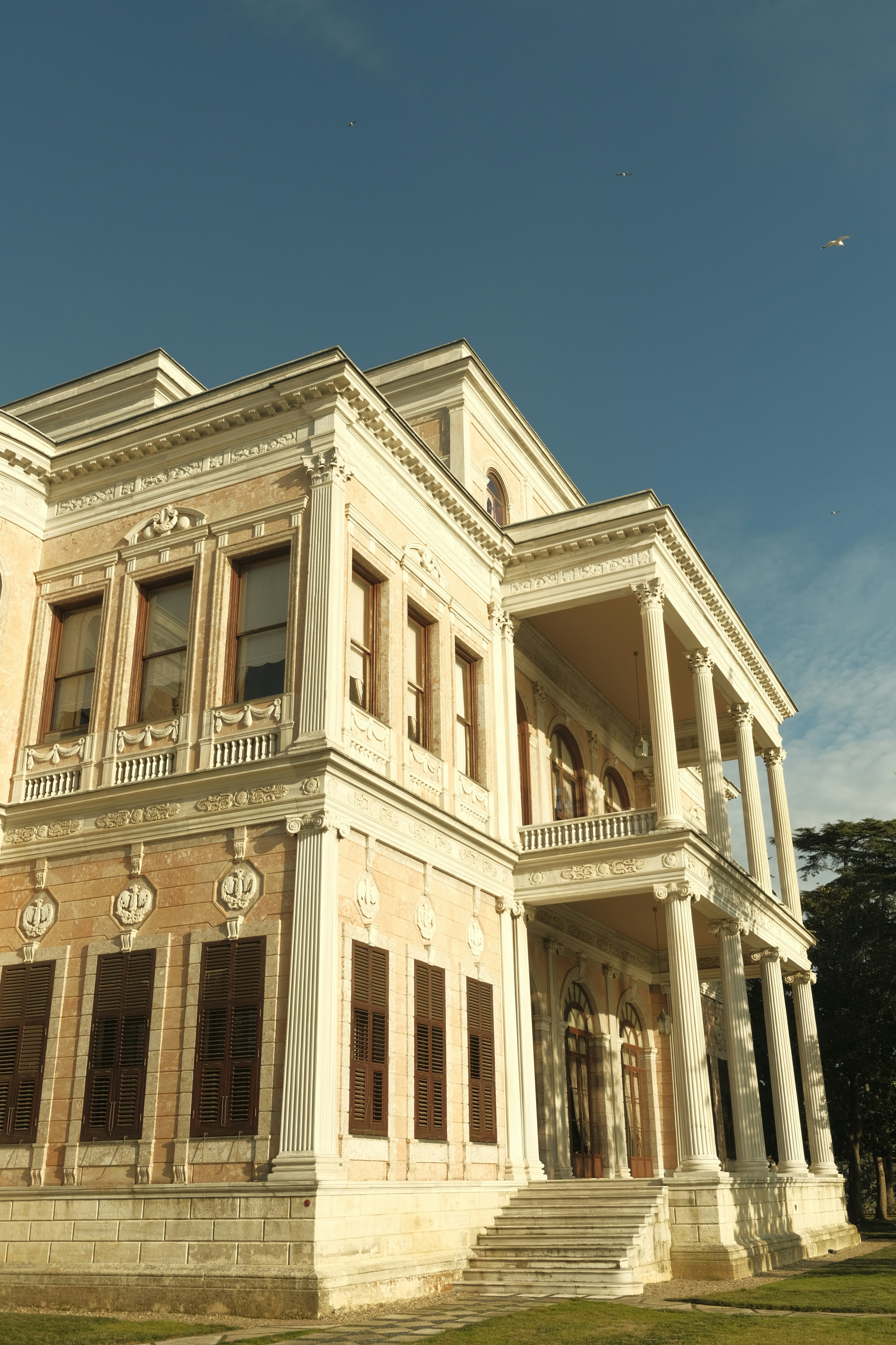 A neoclassical mansion with pale stone walls and dark shutters under a clear sky