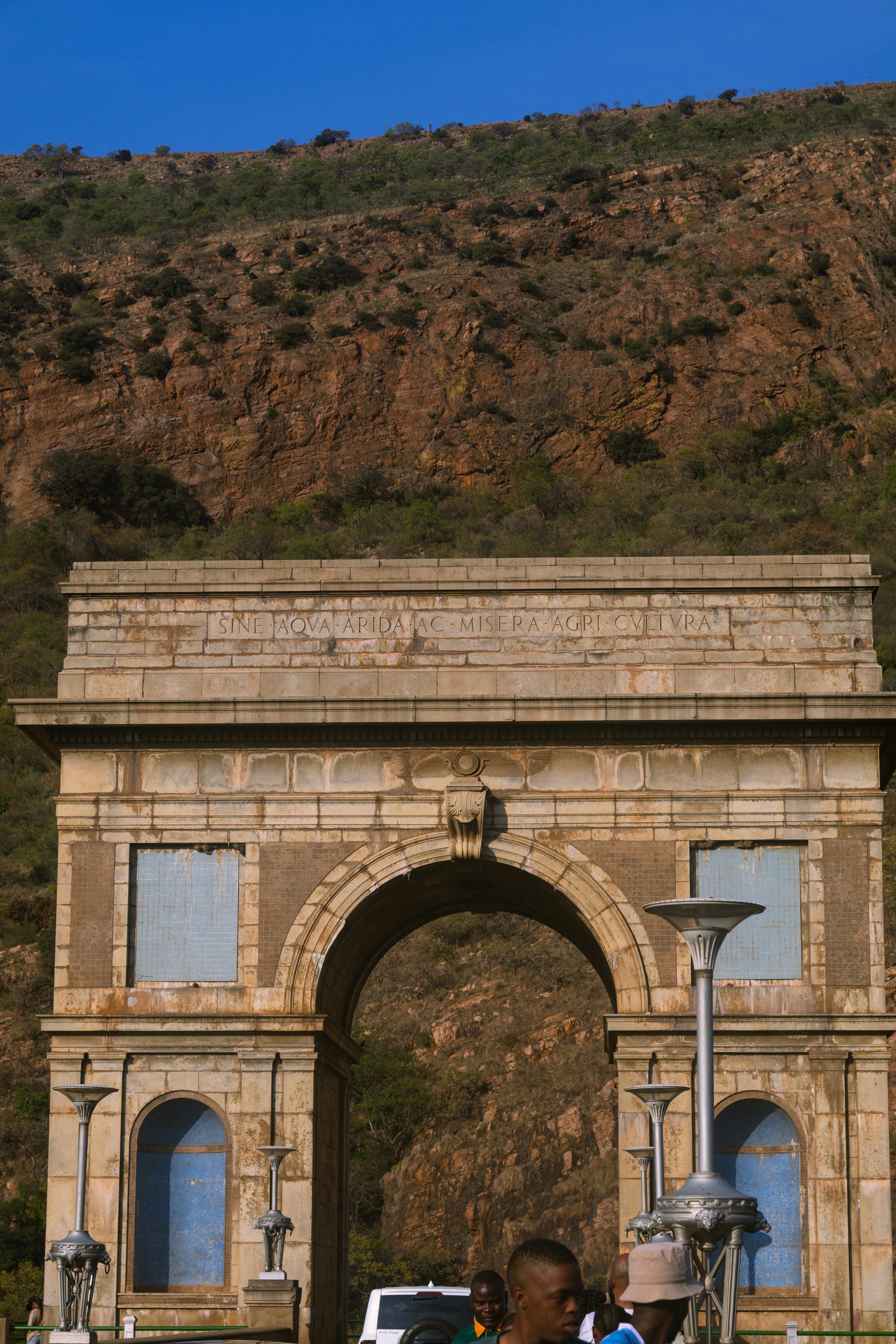 A stone triumphal arch with Latin inscription before a rocky mountain slope