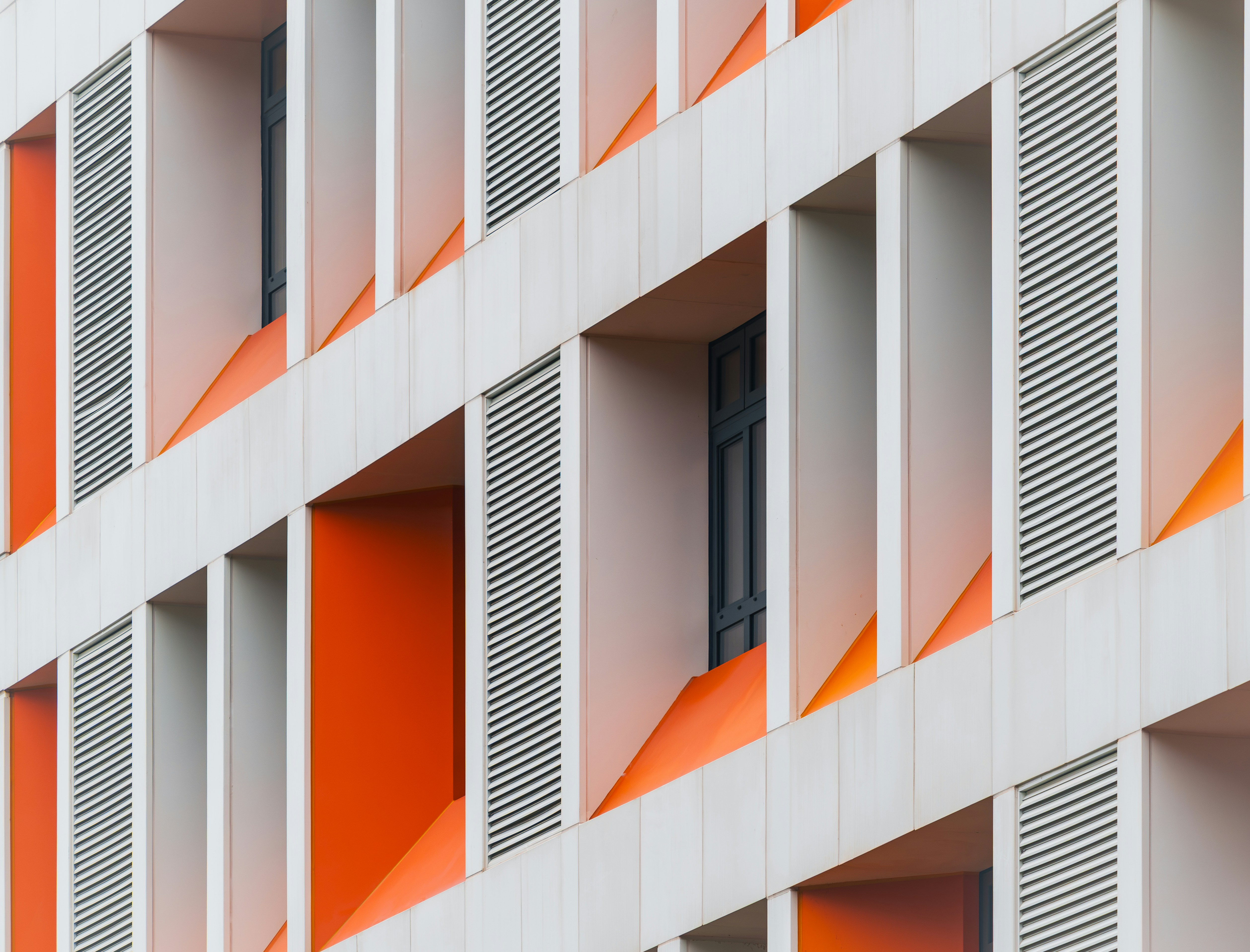Fachada moderna del edificio con paneles blancos, detalles naranjas y contraventanas grises