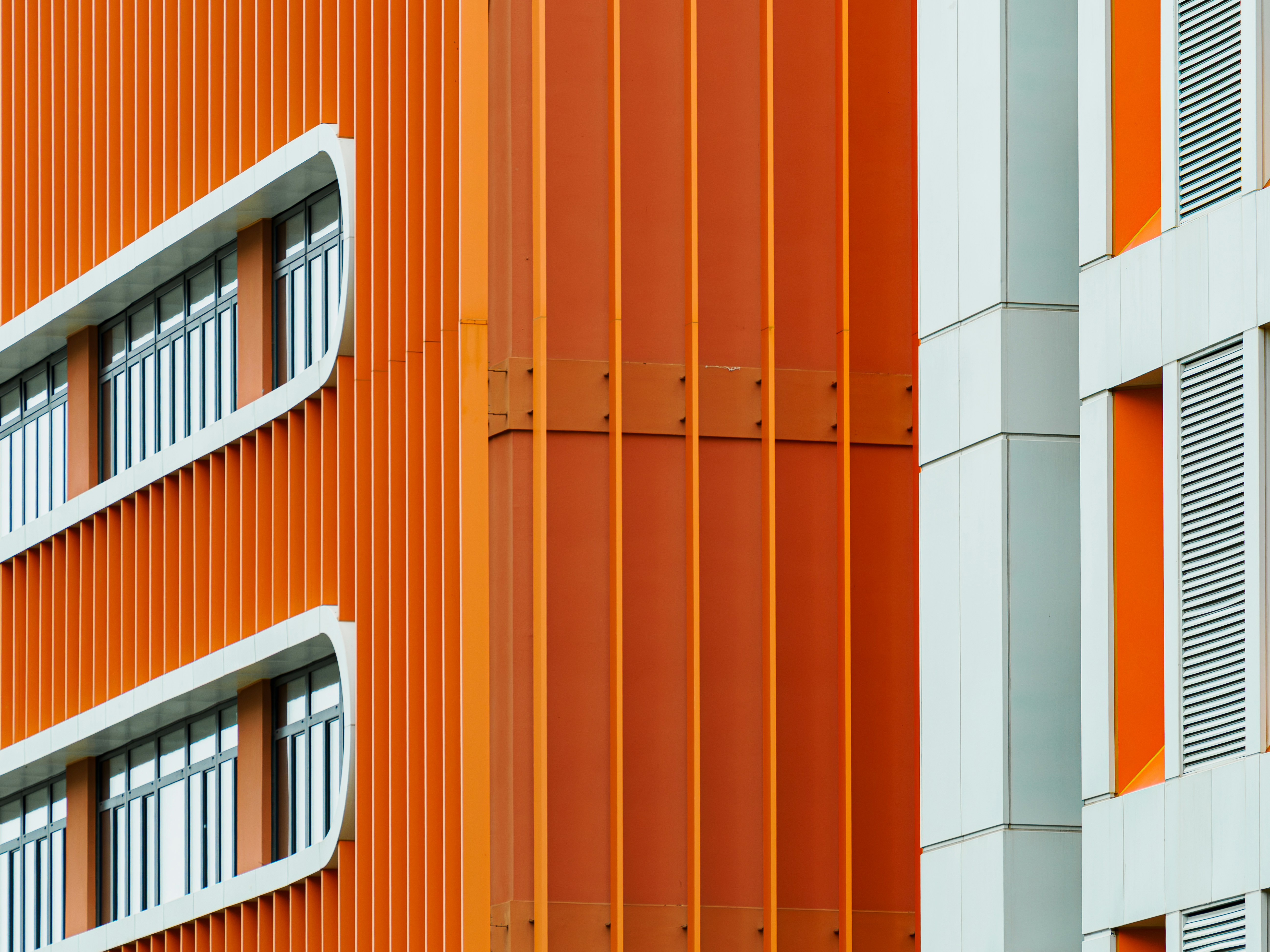 Fachada moderna del edificio con aletas verticales naranjas y marcos de ventanas blancos