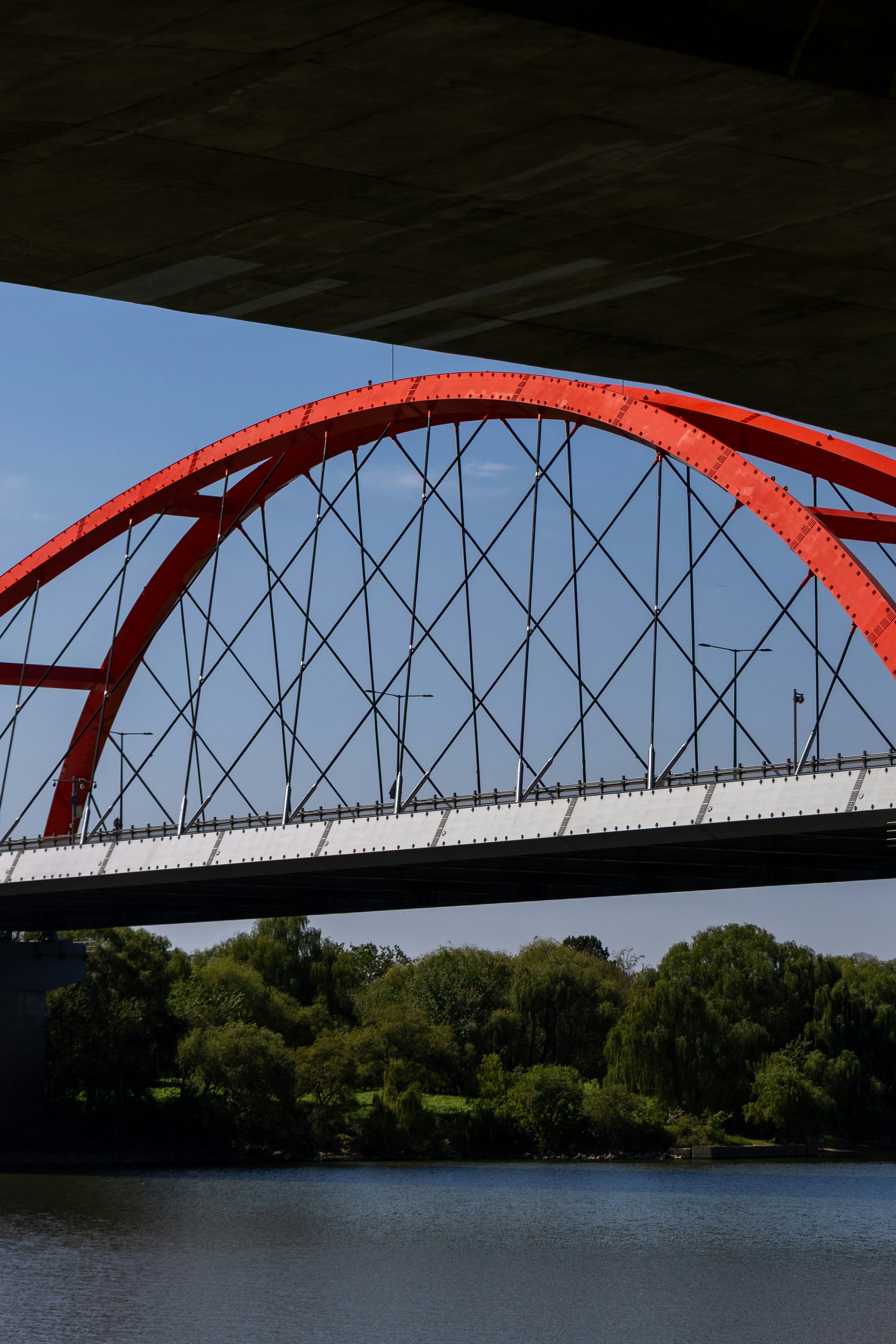 A bright red arched bridge spanning a river with green trees on the bank