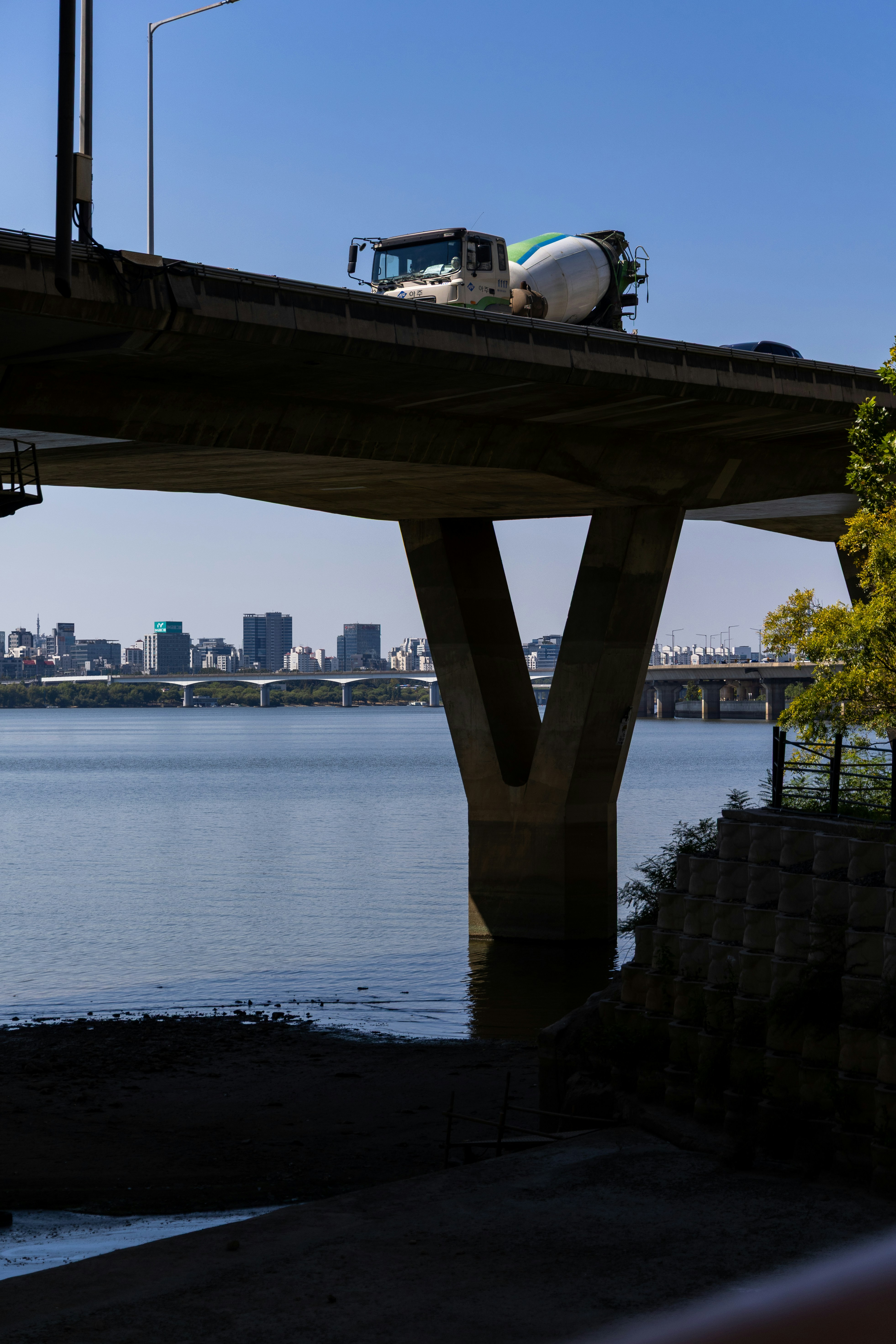 A cement mixer truck driving across a concrete bridge over a wide river