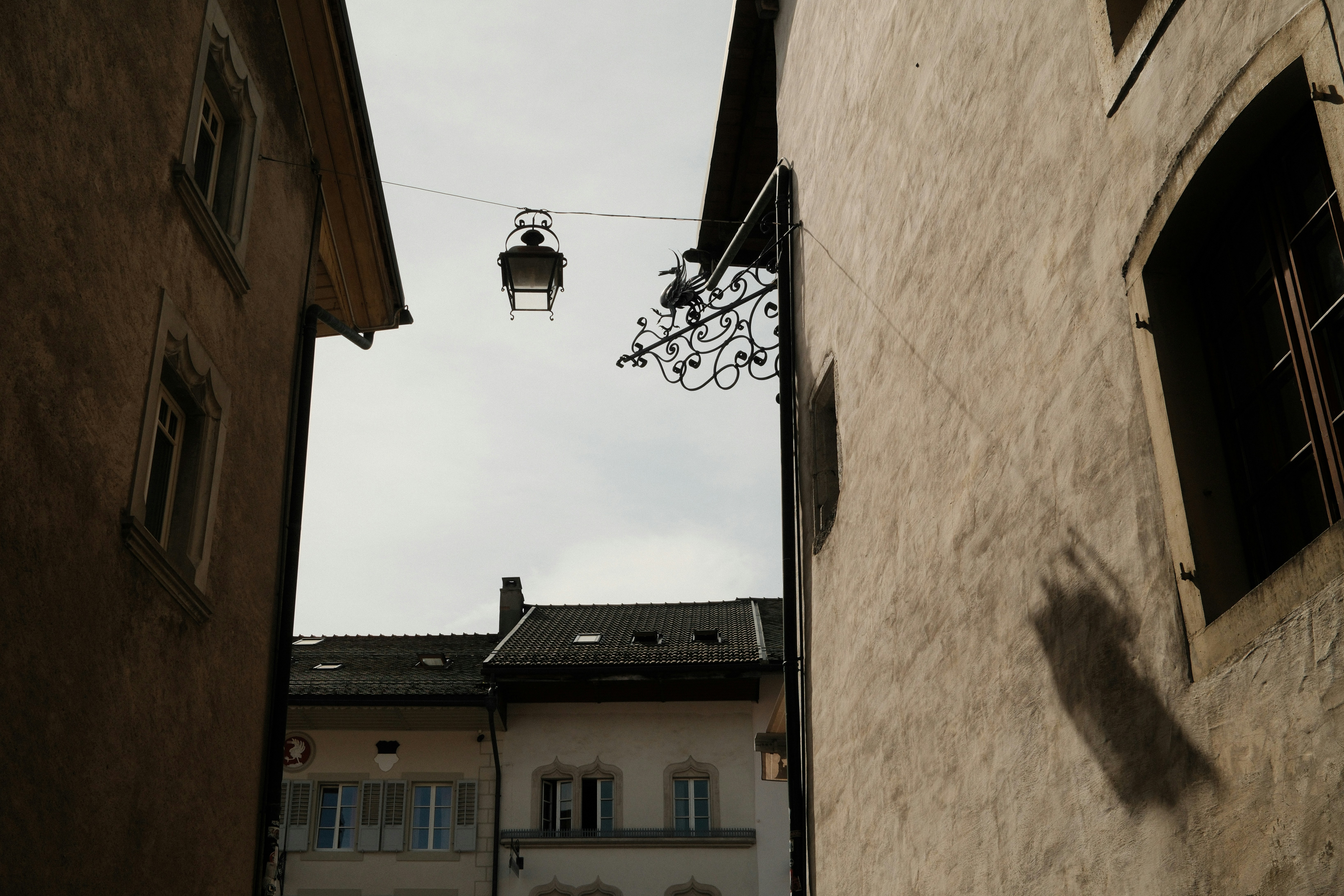 A hanging lantern and ornate metal sign between two old stone buildings