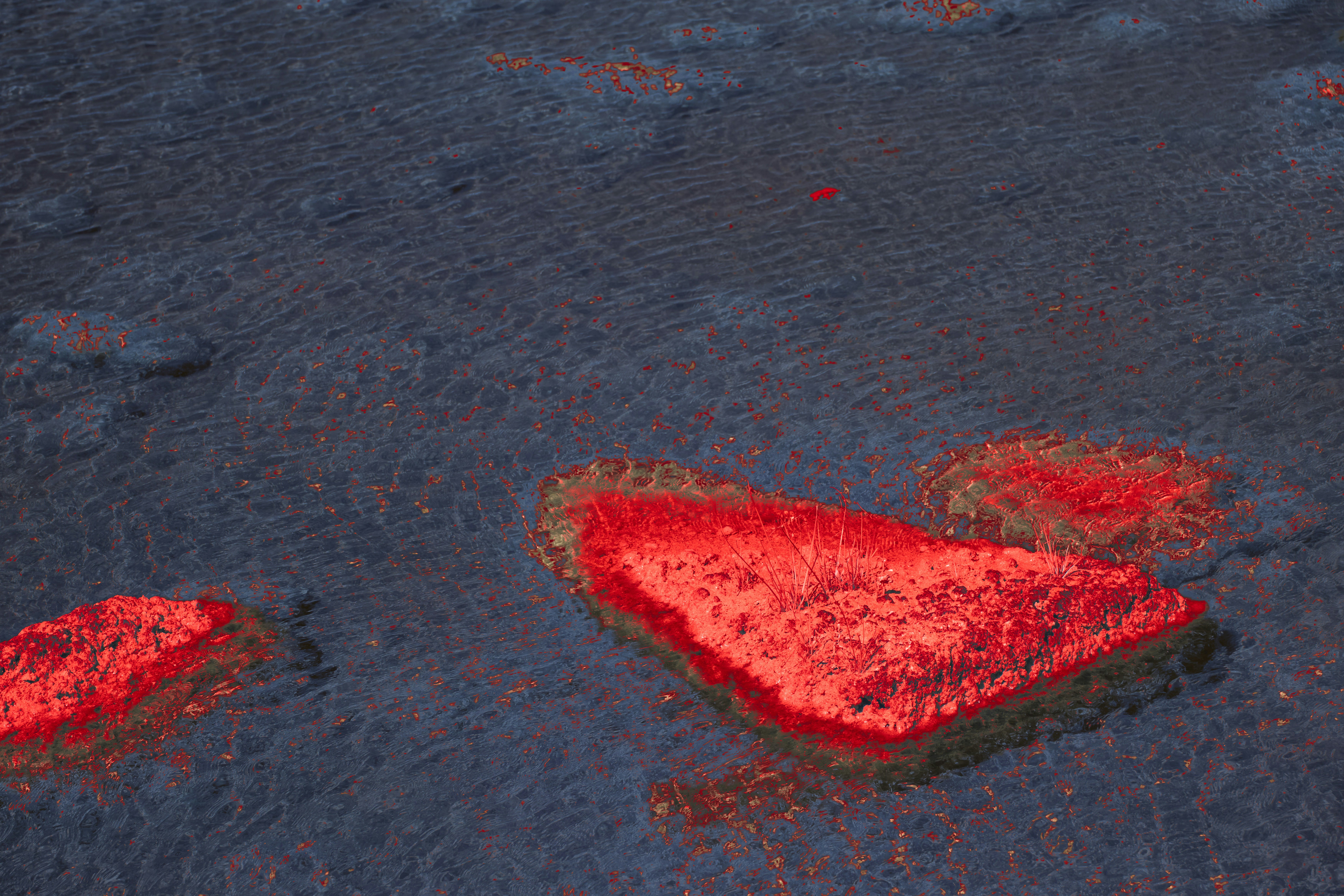 Bright red rocky islands in dark rippling water