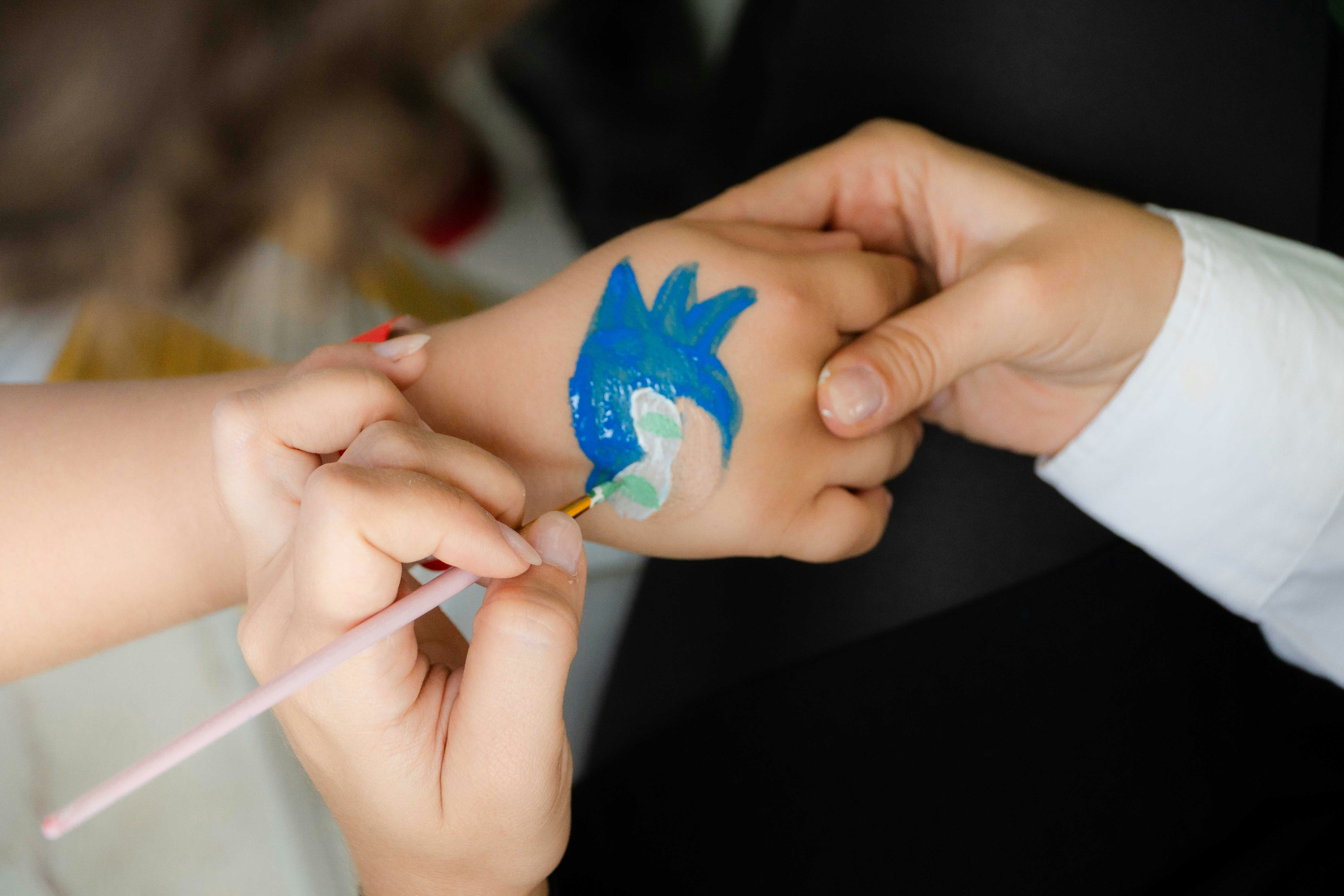 A person painting a blue cartoon character on a child's hand with a brush