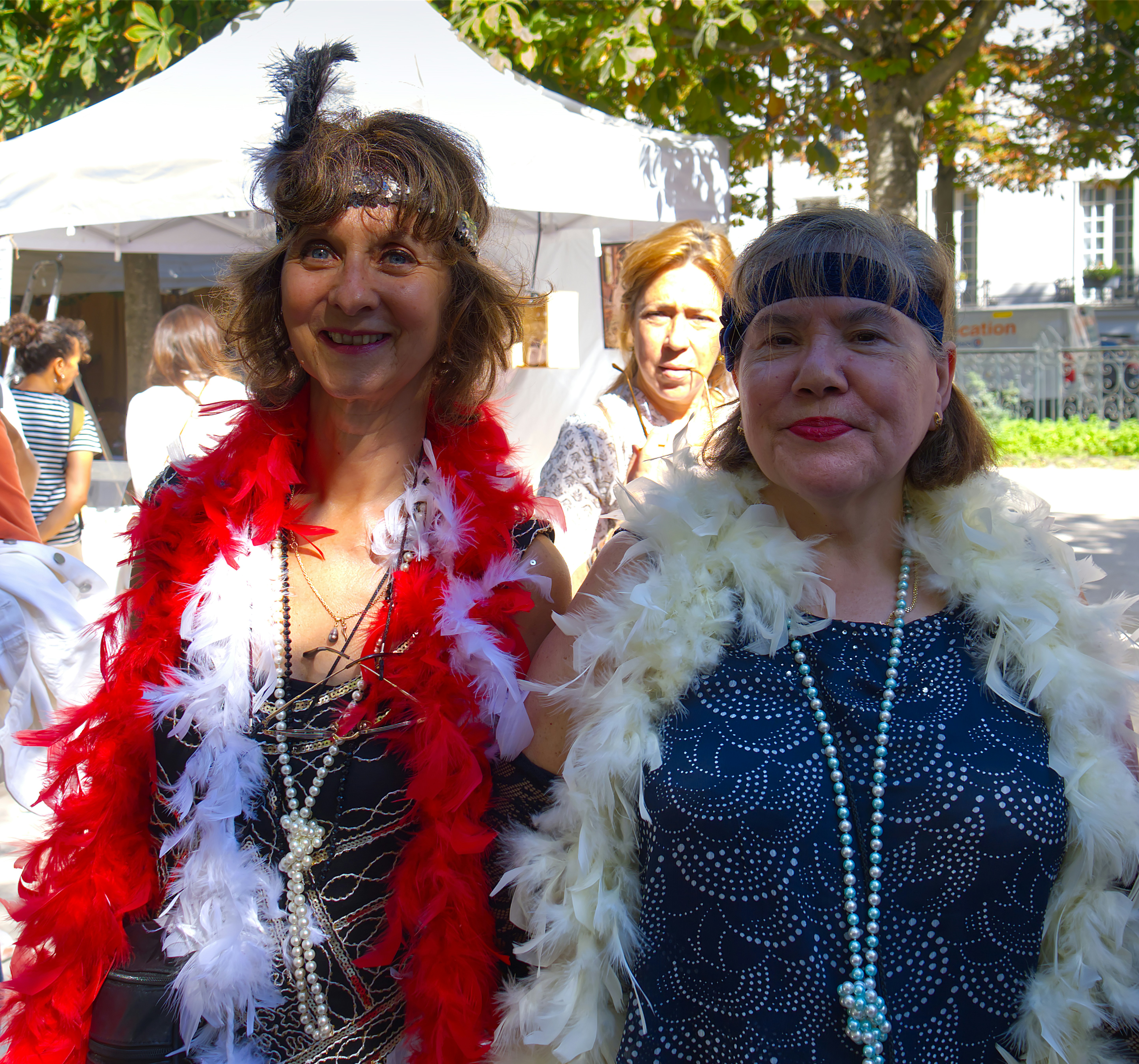Two women in flapper-style headbands and feather boas at an outdoor event