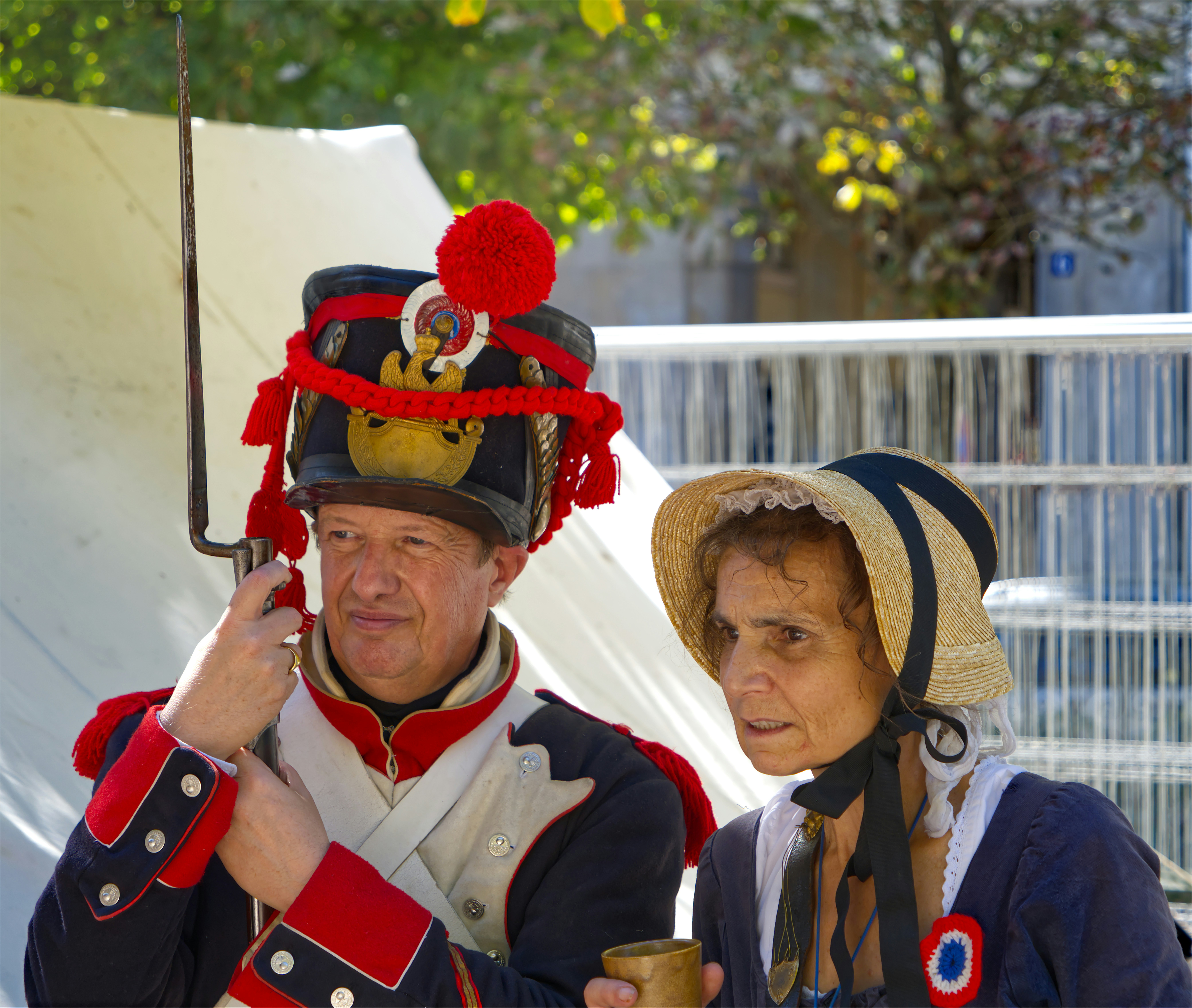 A man in a Napoleonic uniform holding a bayonet beside a woman in a bonnet