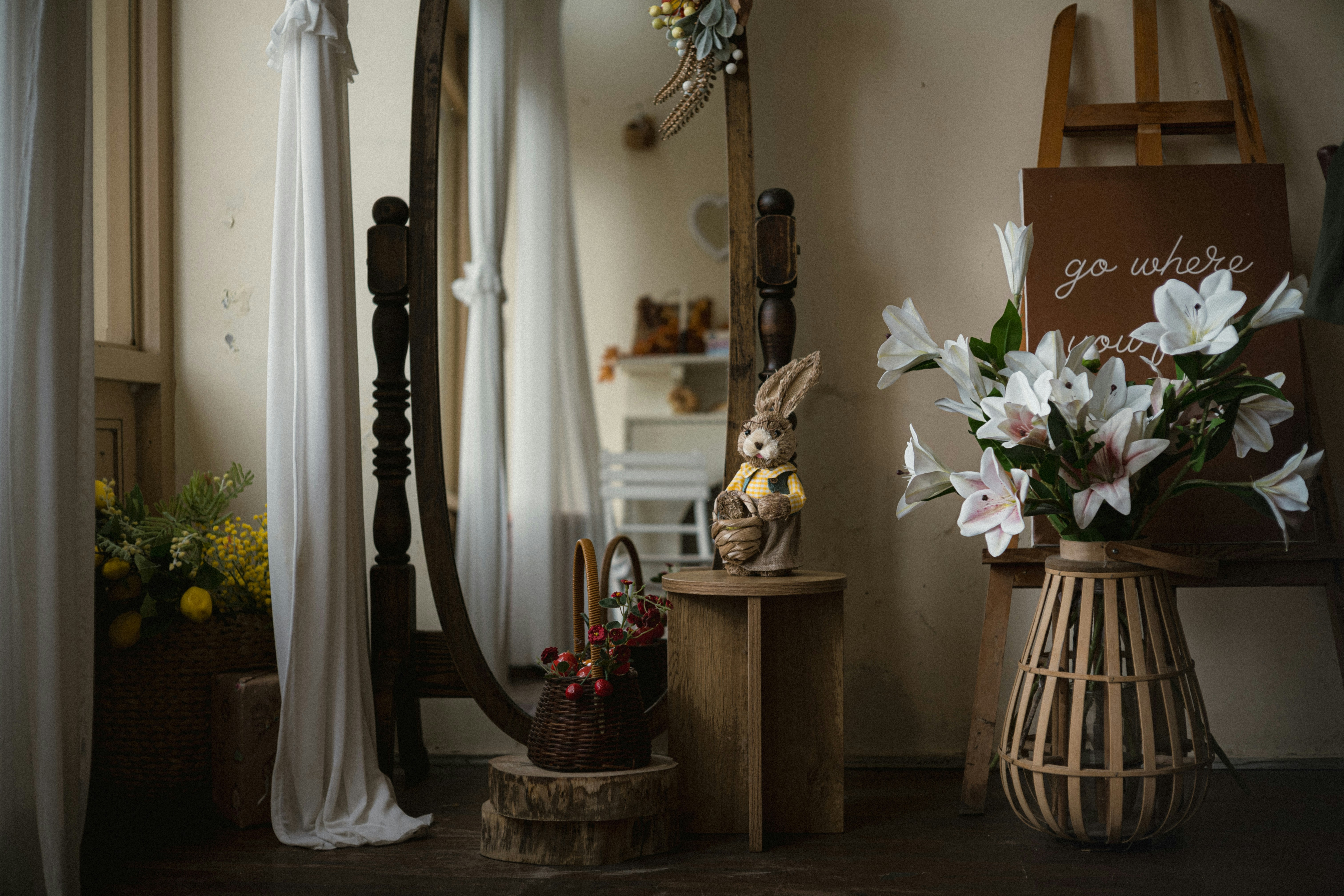 A toy rabbit on a wooden stool beside white lilies in a basket