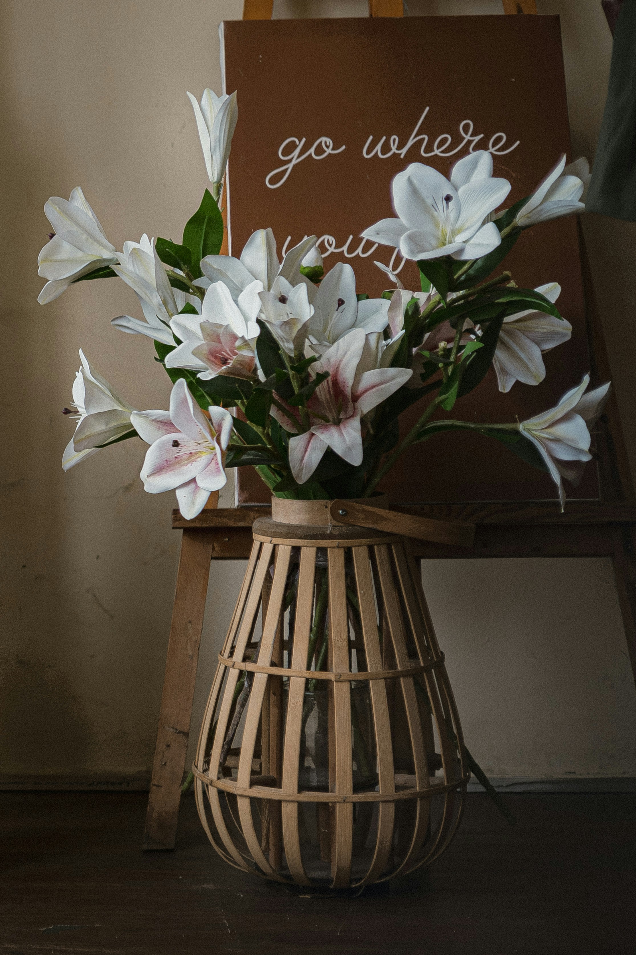 White lilies in a wooden slatted vase on a wooden easel