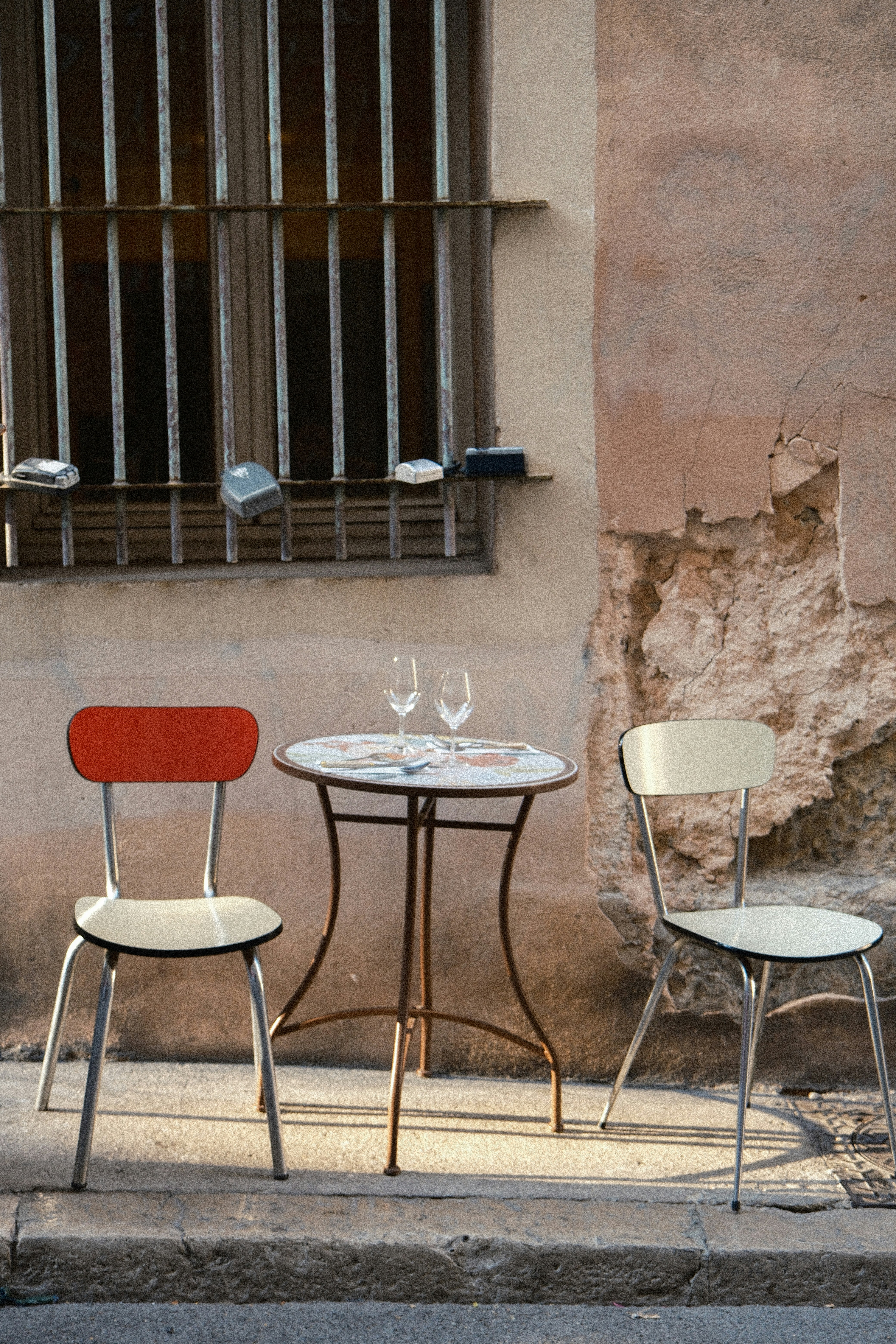 A small round table with two chairs on a sidewalk against a weathered wall