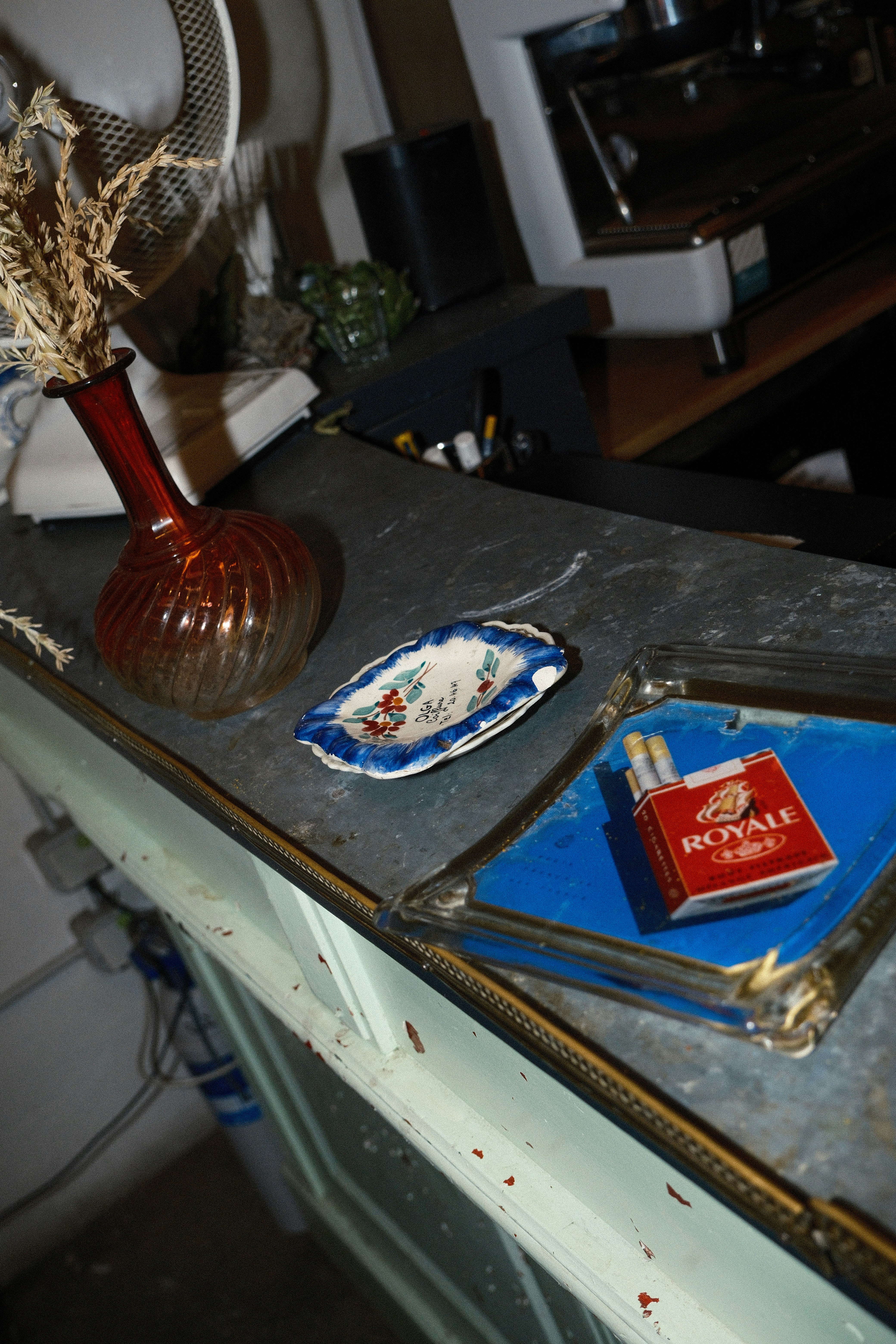 A red glass vase, a small decorative dish, and cigarettes on a counter