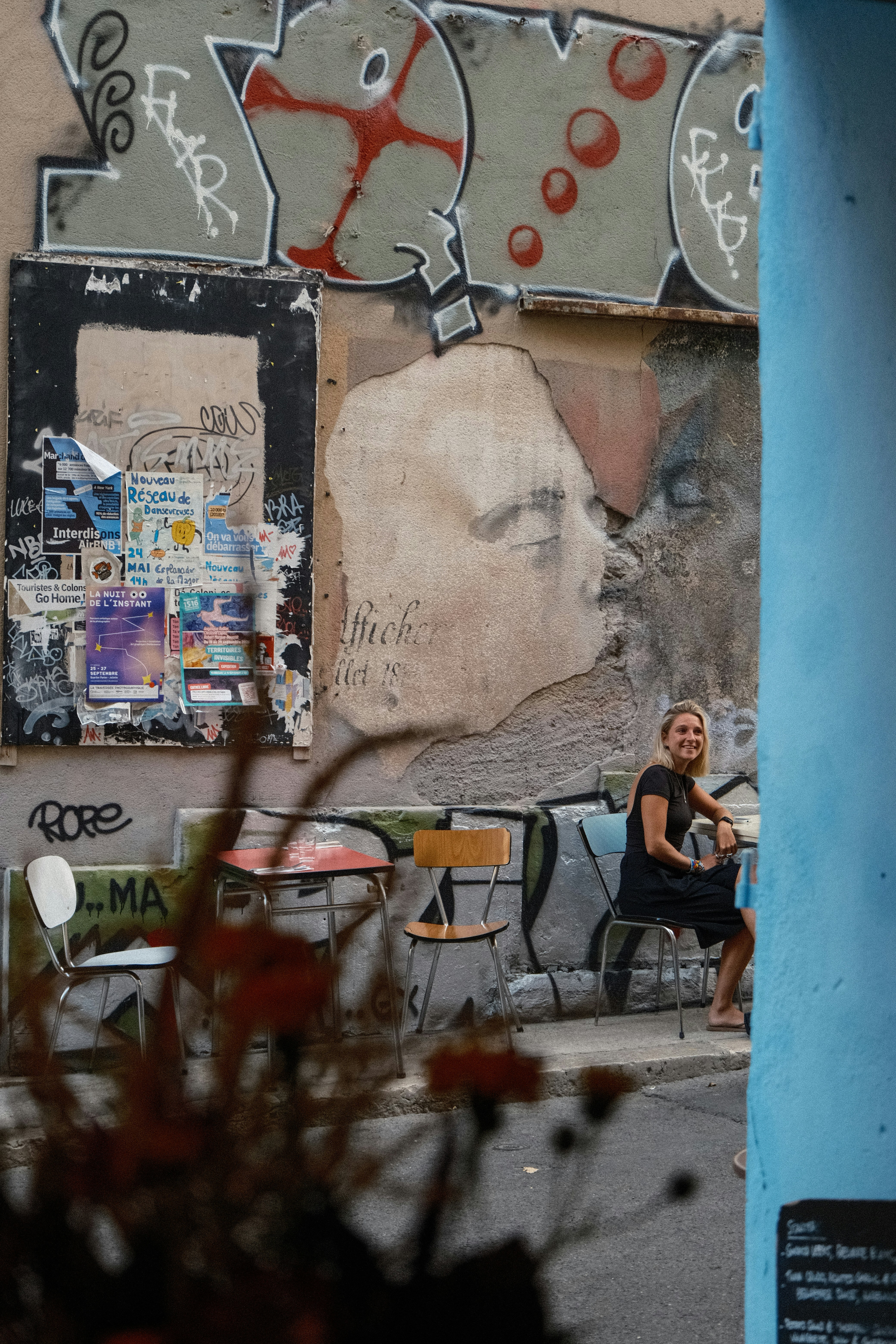 A woman sitting at a small table against a graffiti covered wall