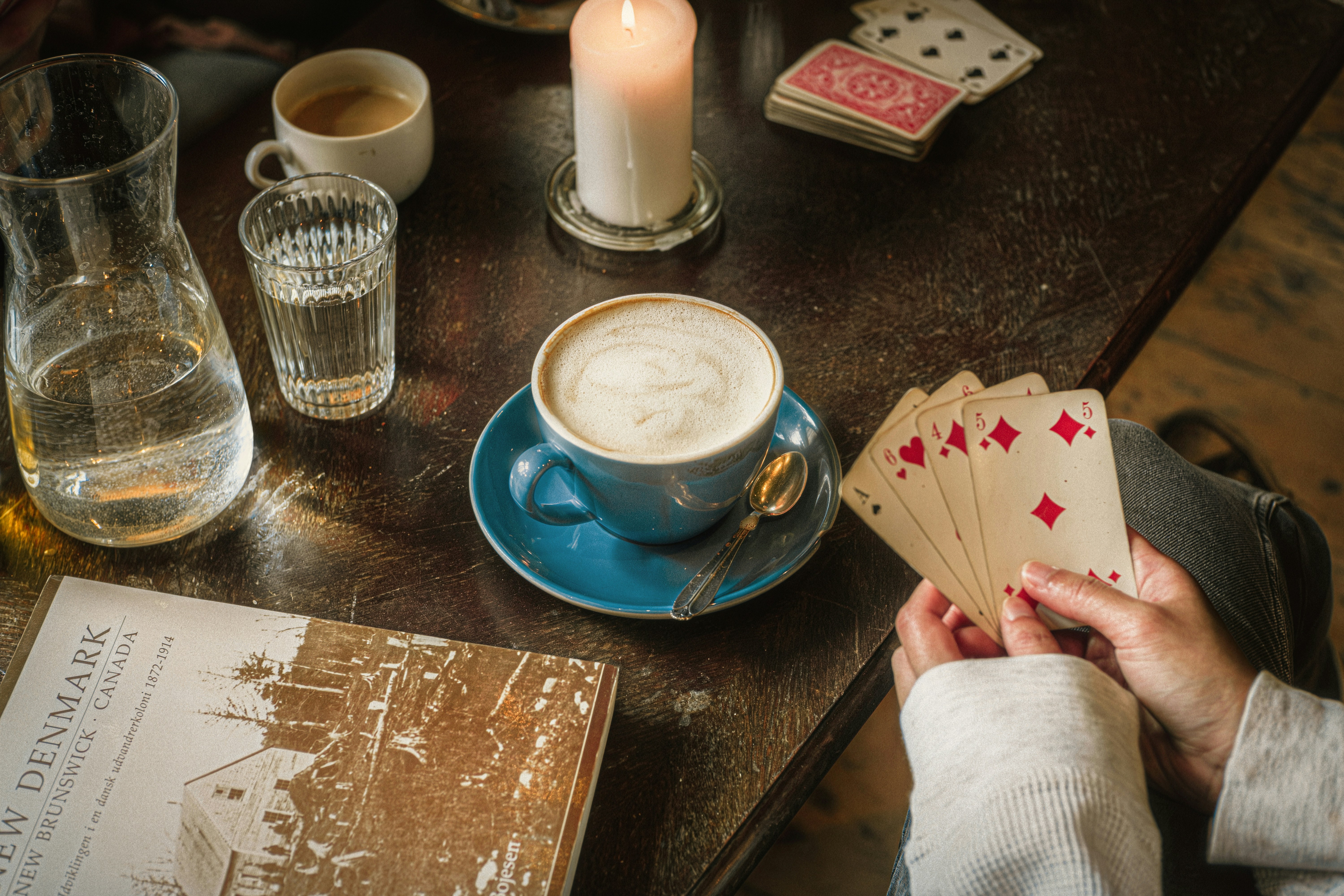 Una persona che tiene carte da gioco accanto a una tazza di caffè su un tavolo di legno
