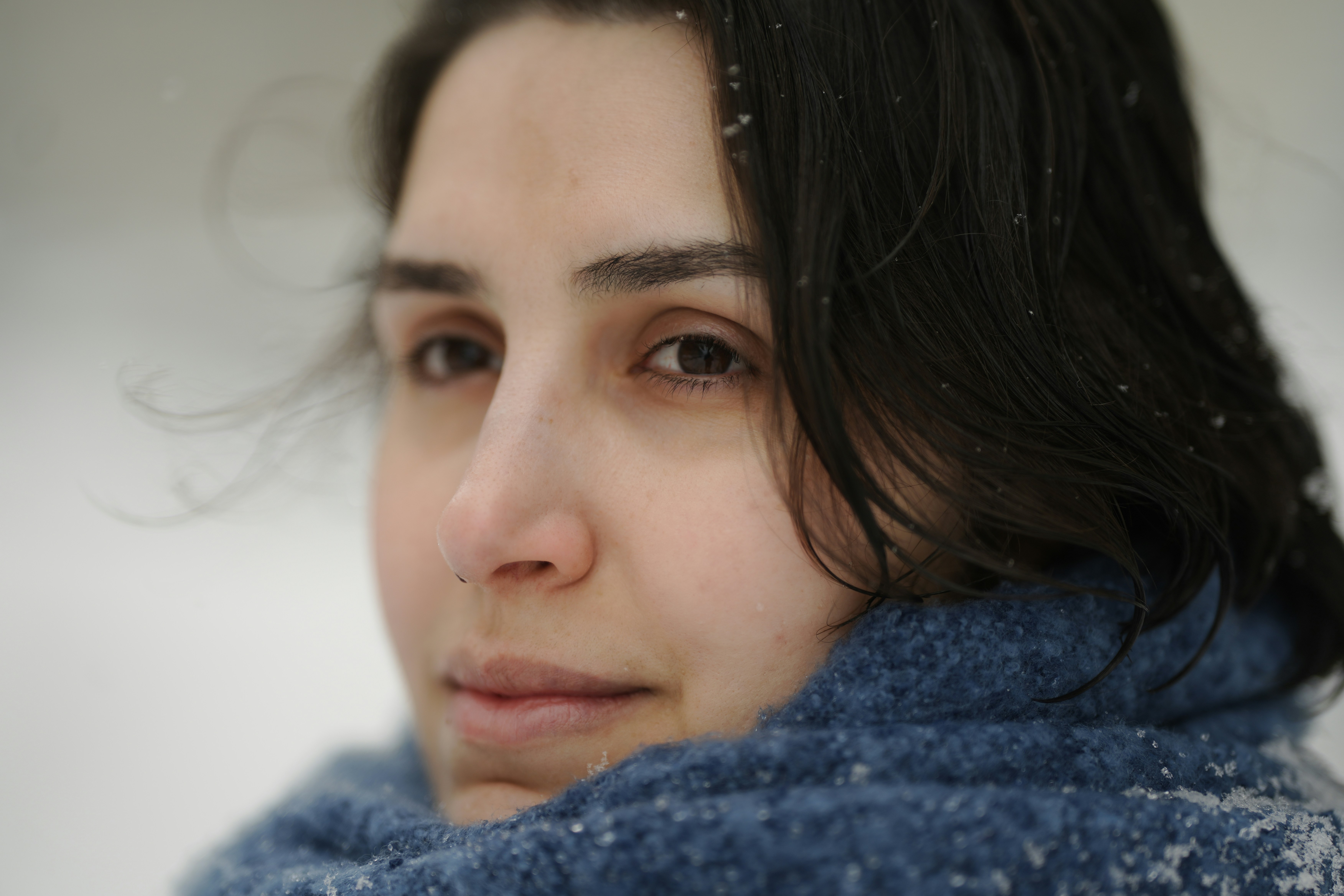 A woman with dark hair wearing a blue knitted scarf in the snow