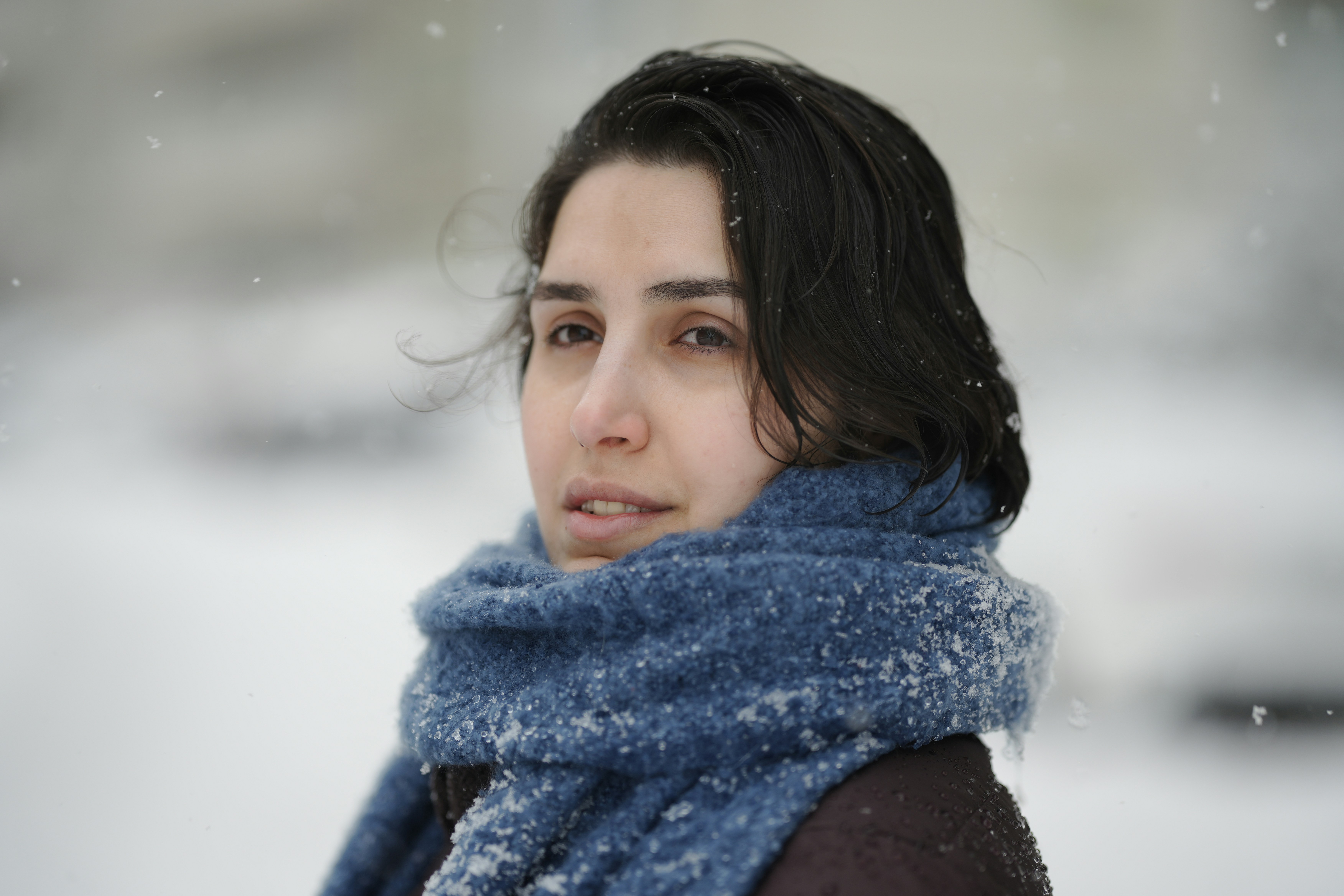 A woman with dark hair wearing a blue knitted scarf during a snowfall