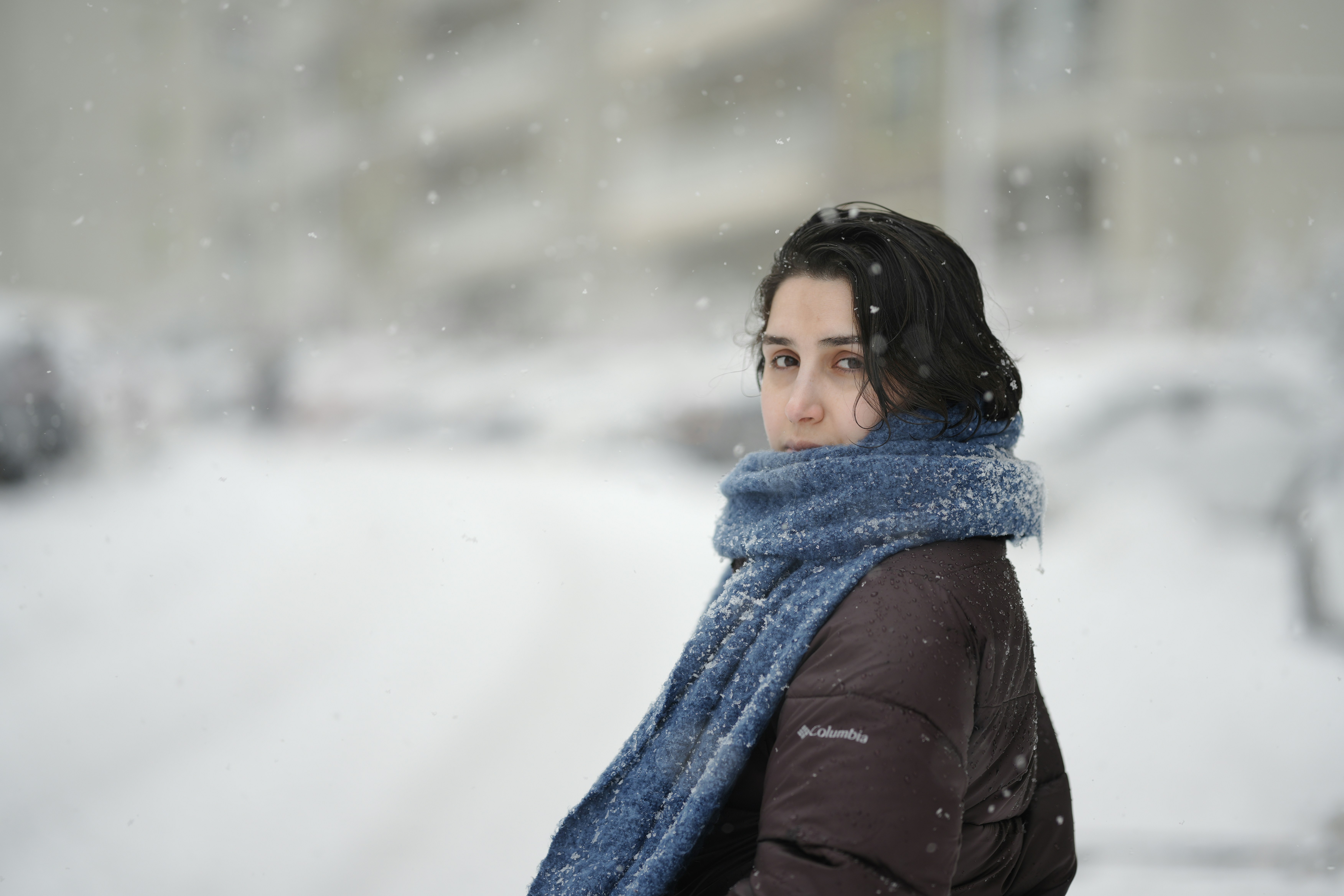 Uma mulher de jaqueta escura e cachecol azul durante uma queda de neve