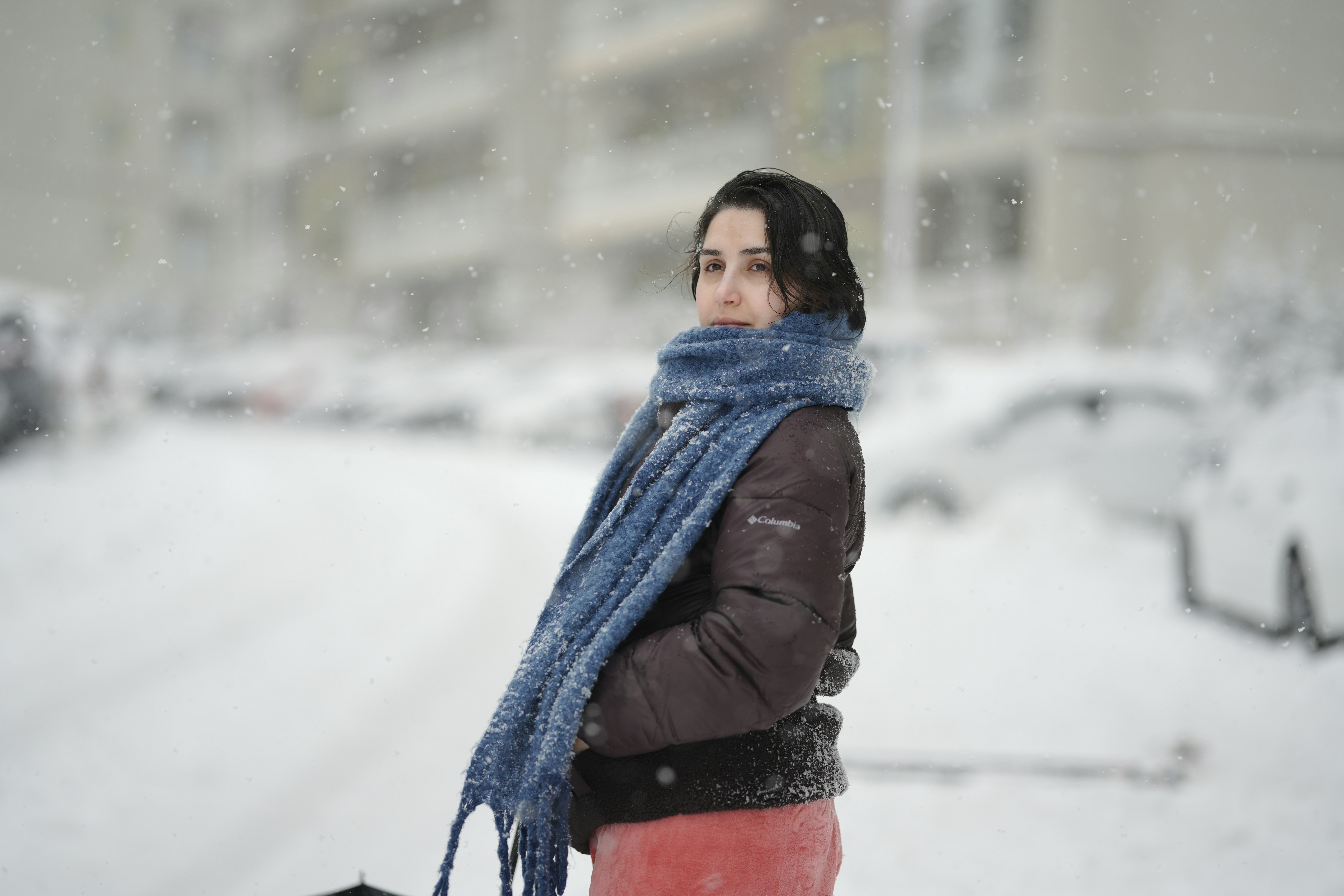 A woman in a dark jacket and blue scarf during a snowstorm