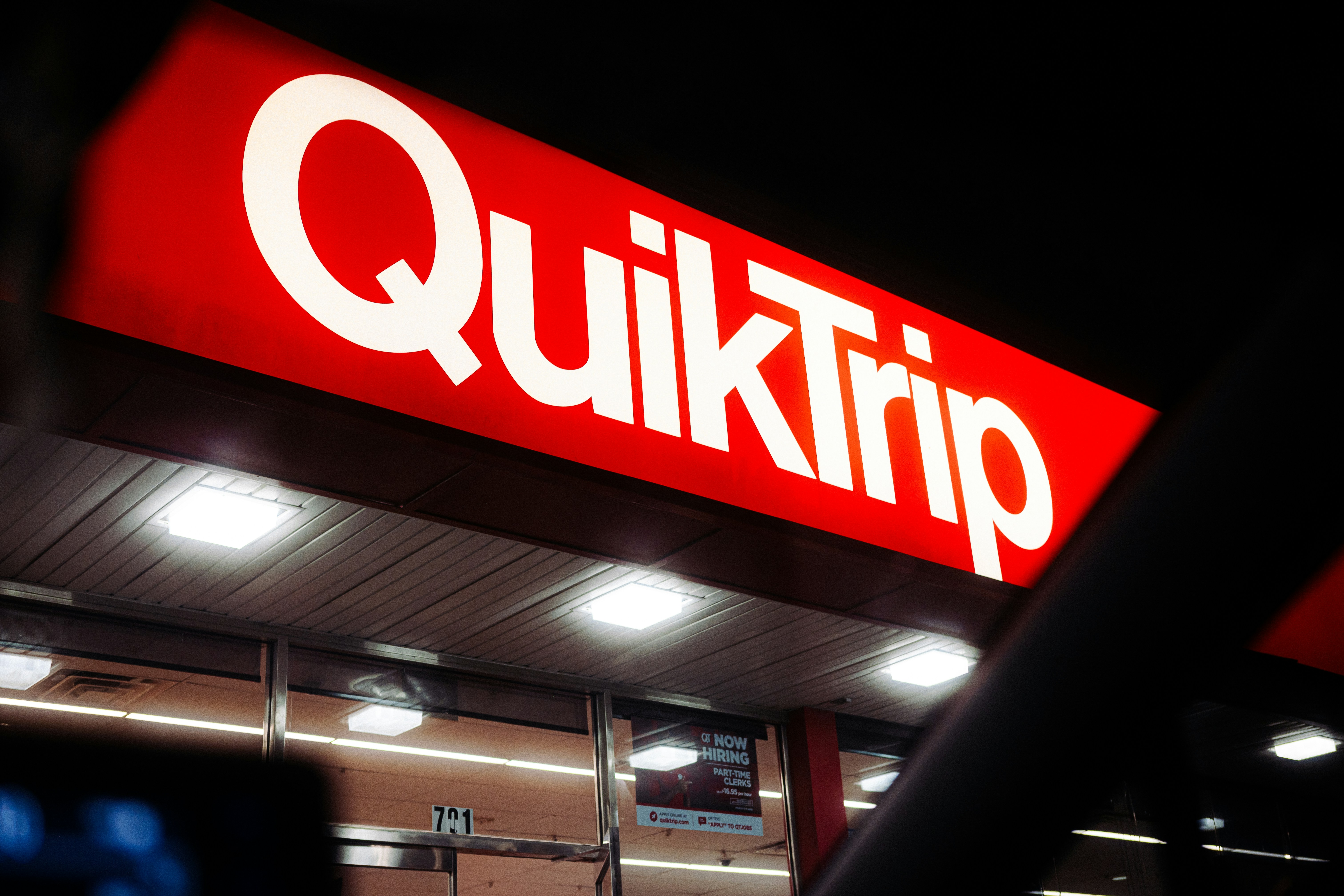 Ein knallrot beleuchtetes Schild mit der Aufschrift QuikTrip über einem Eingang eines Convenience Stores bei Nacht
