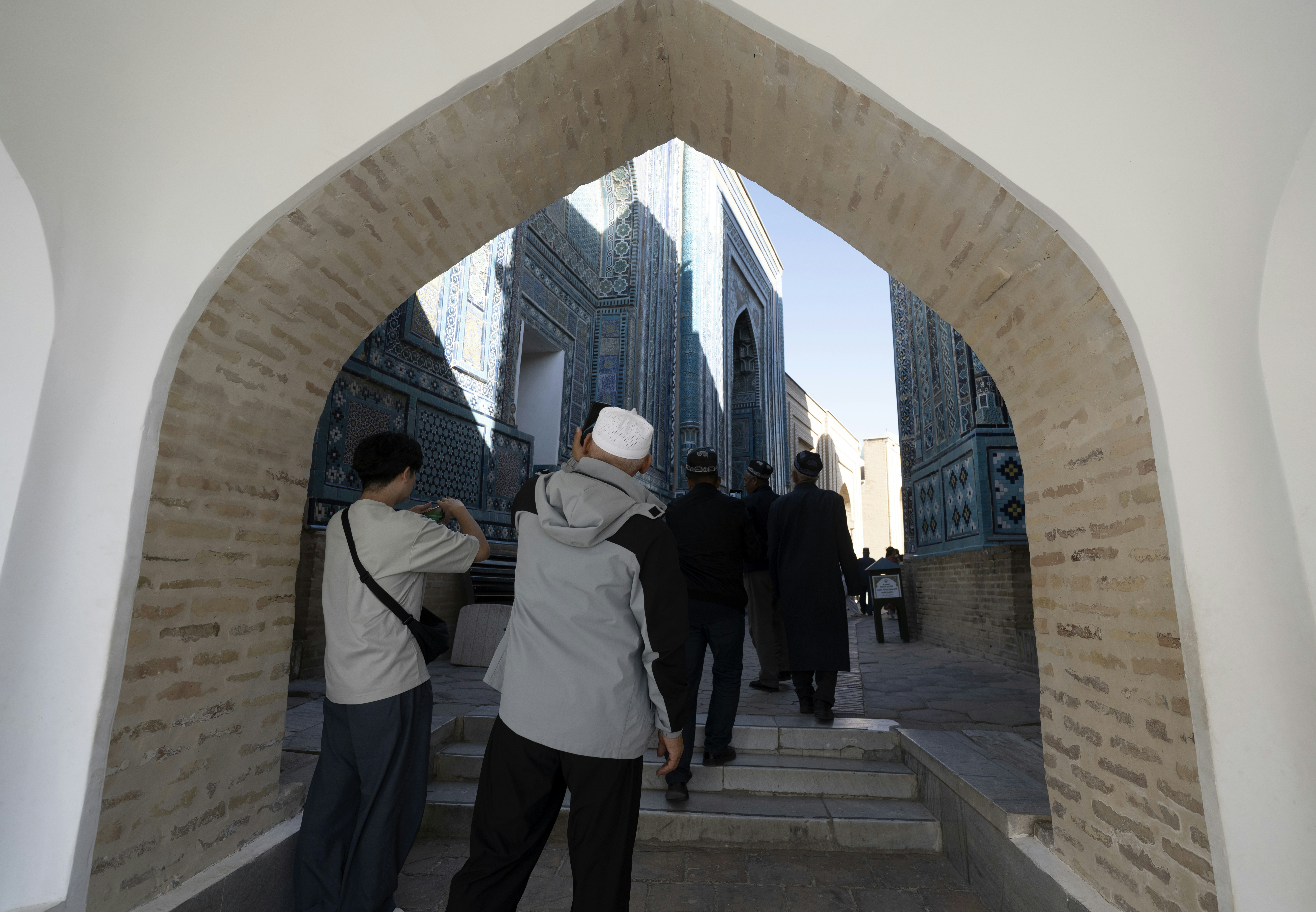 People walking through a stone archway toward blue tiled buildings in Samarkand