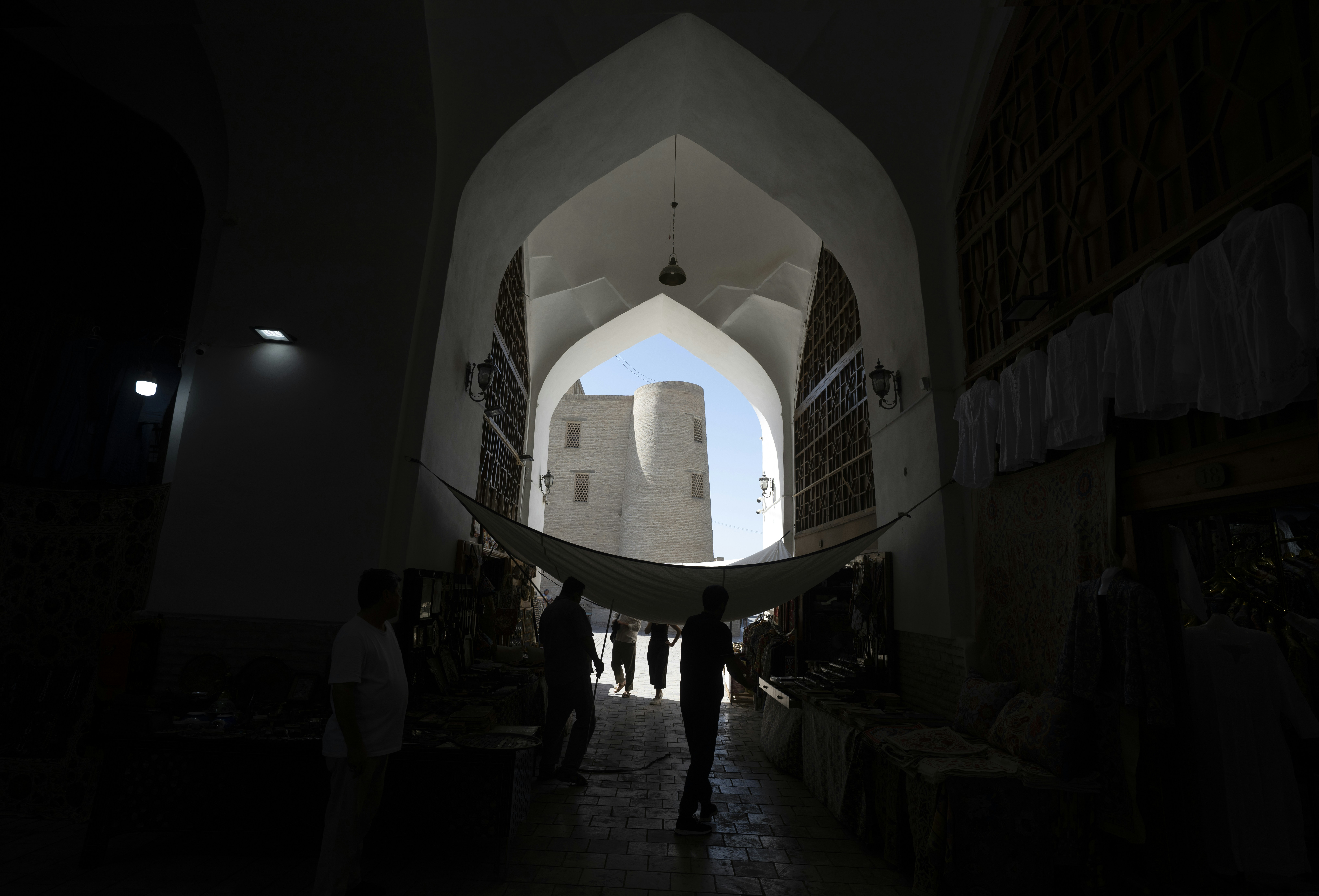 Silhouetted people in a shaded stone archway looking toward a sunlit historic tower