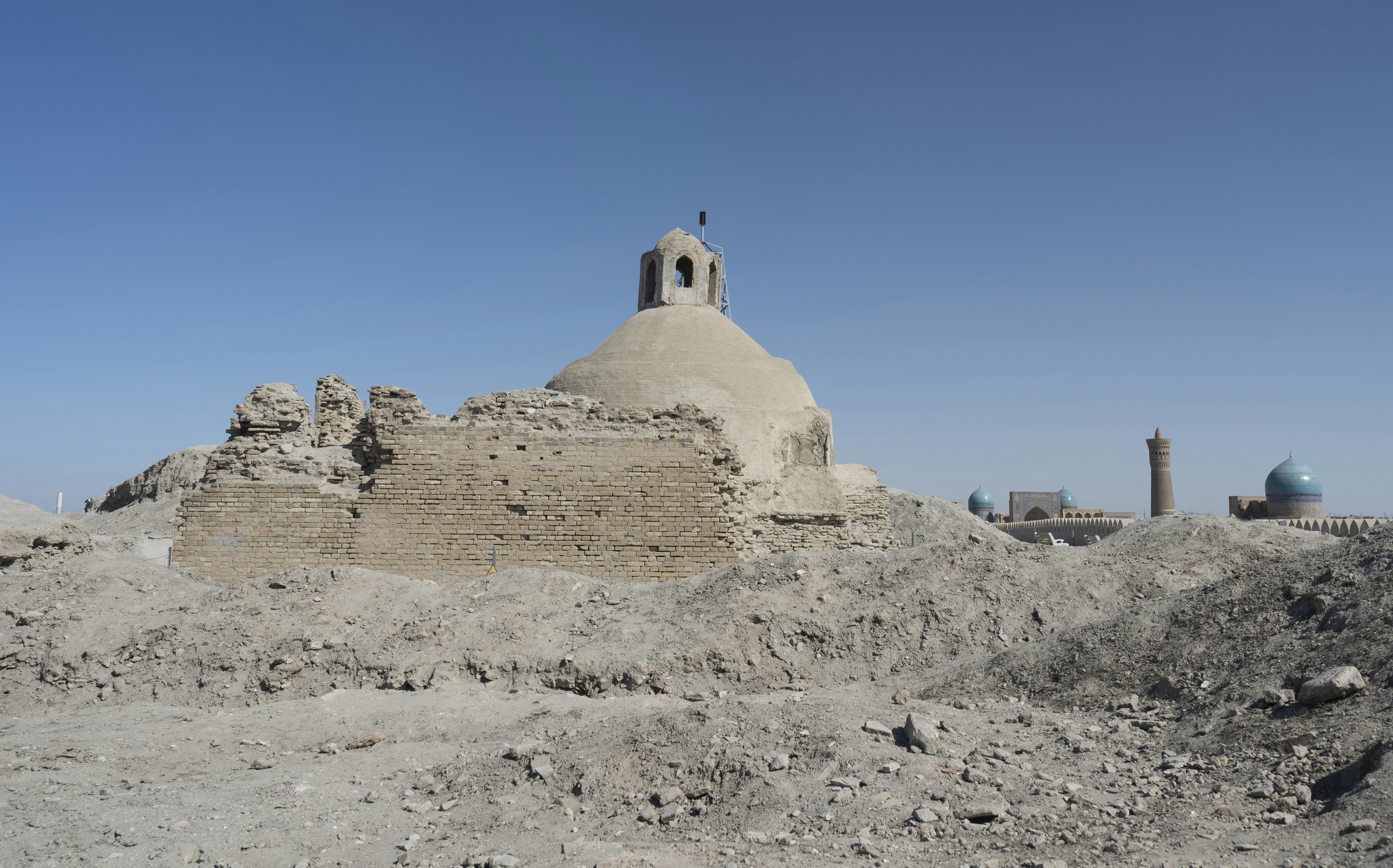 An ancient brick dome structure surrounded by mounds of earth under a clear sky