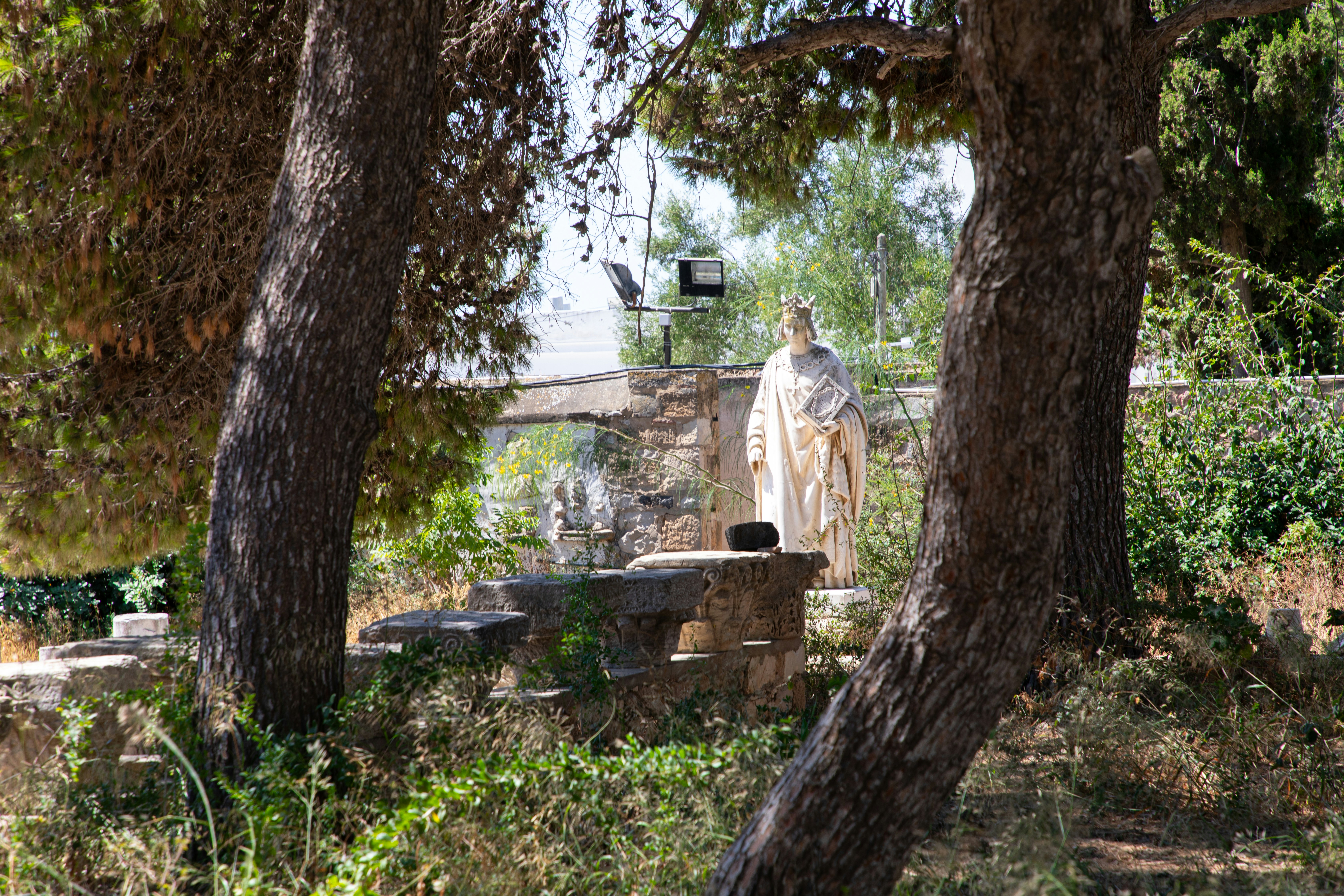 A stone statue of a crowned figure holding a book in a garden
