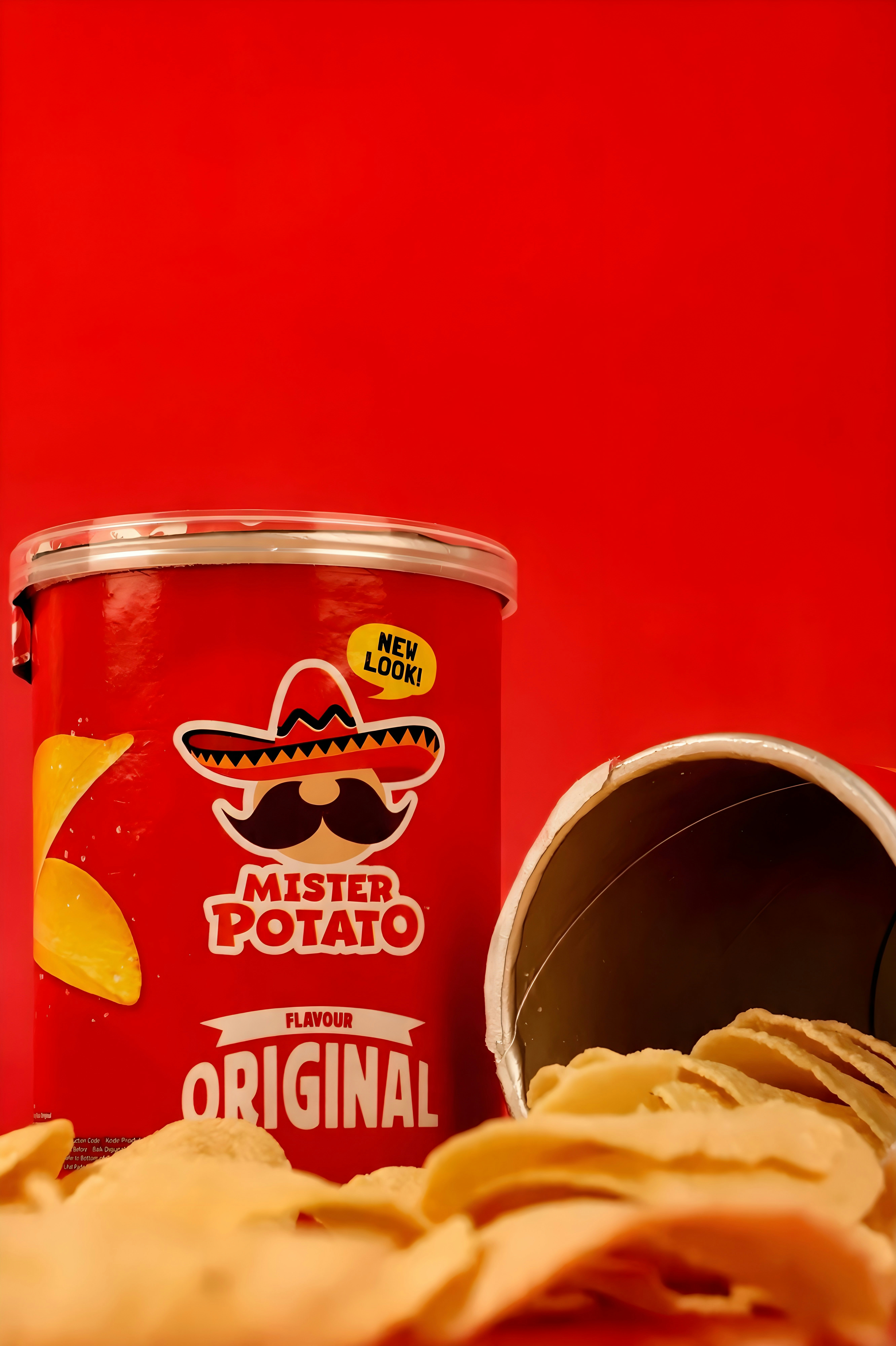 A red Mister Potato snack canister with chips spilling out on a red background