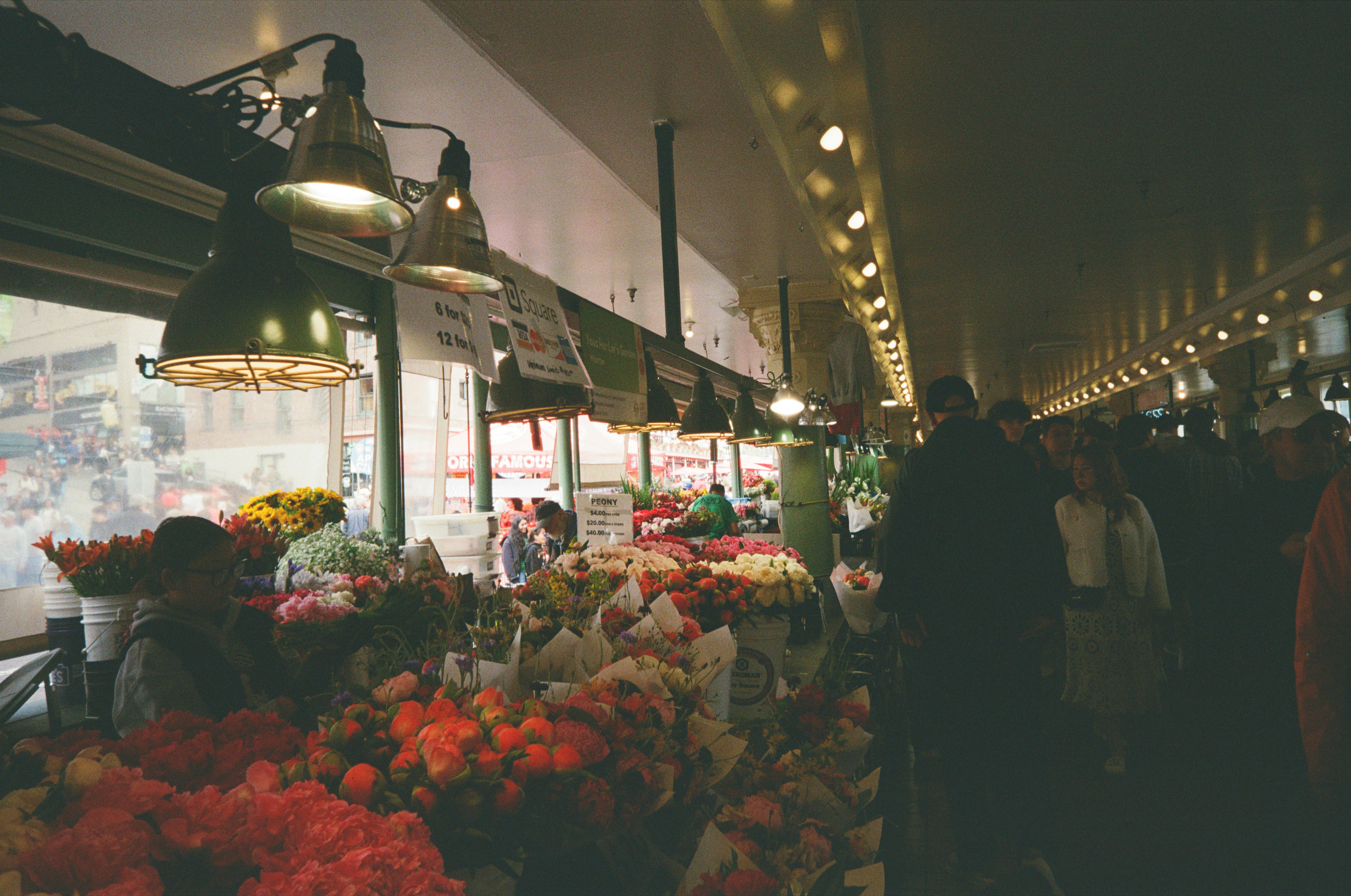 People browsing colorful flower bouquets at a market stall under hanging metal lamps