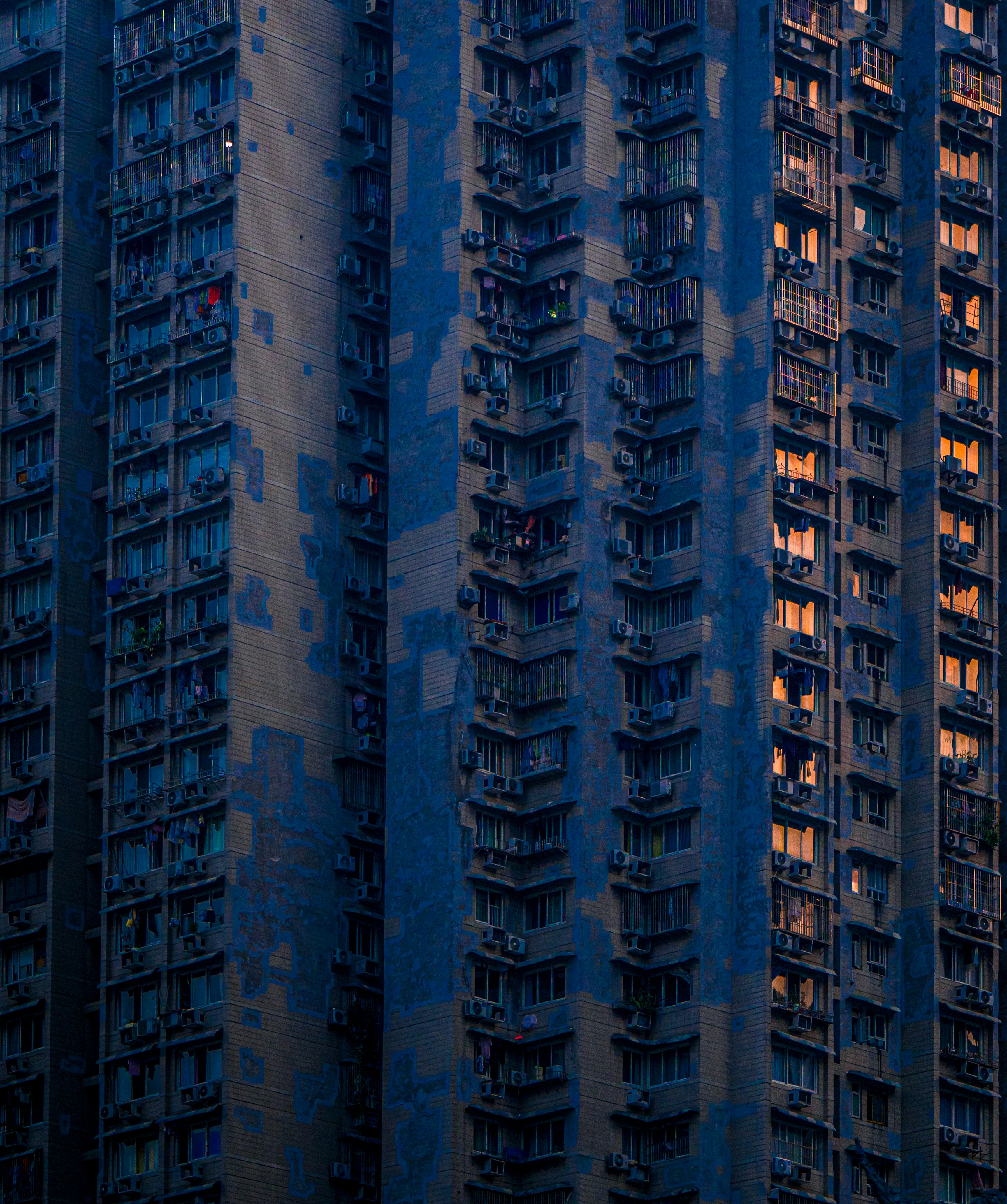 A tall residential apartment building with blue facades and glowing windows at dusk