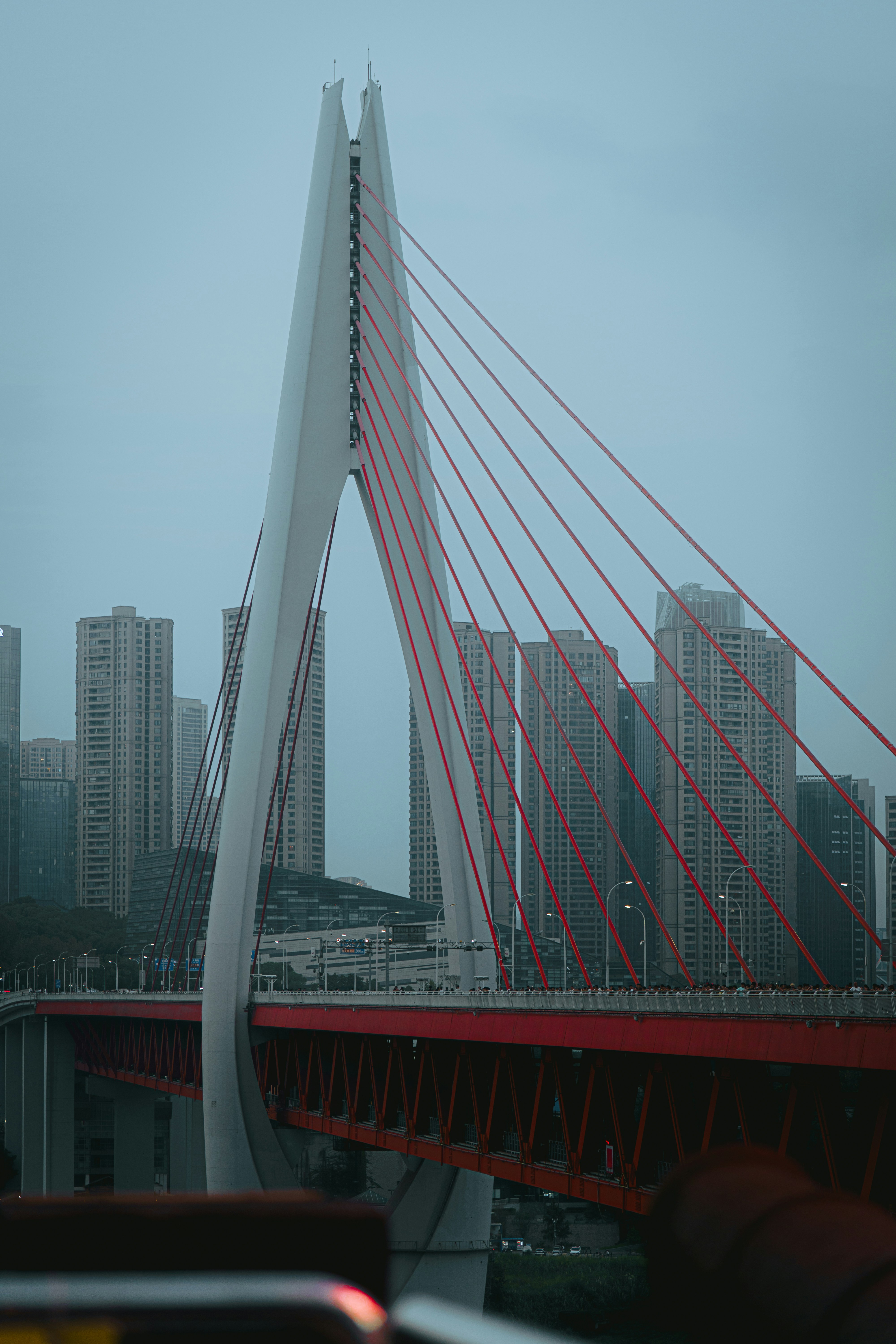 A white cable-stayed bridge with red supports against a backdrop of city skyscrapers