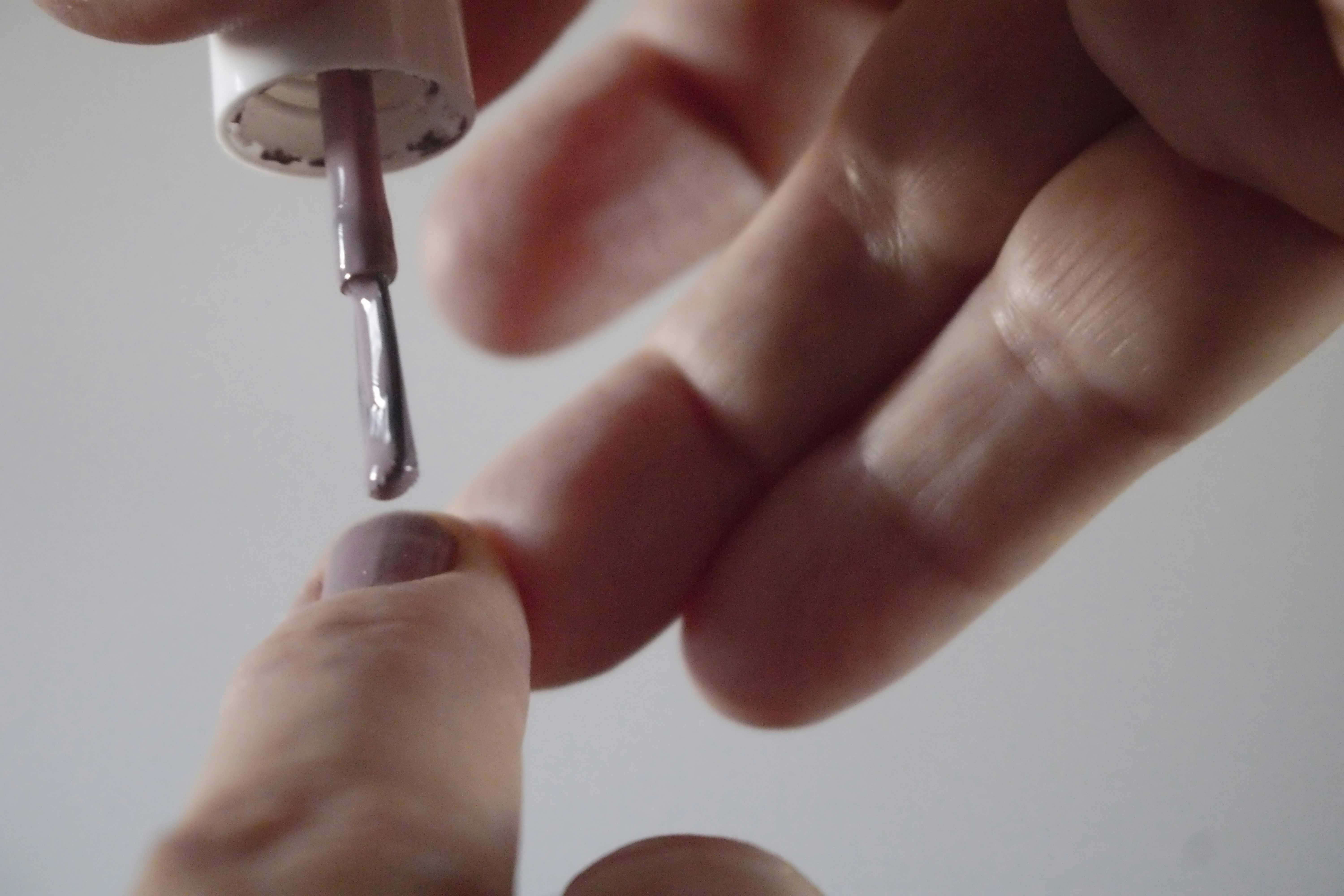 A person applying light purple nail polish to a fingernail with a small brush