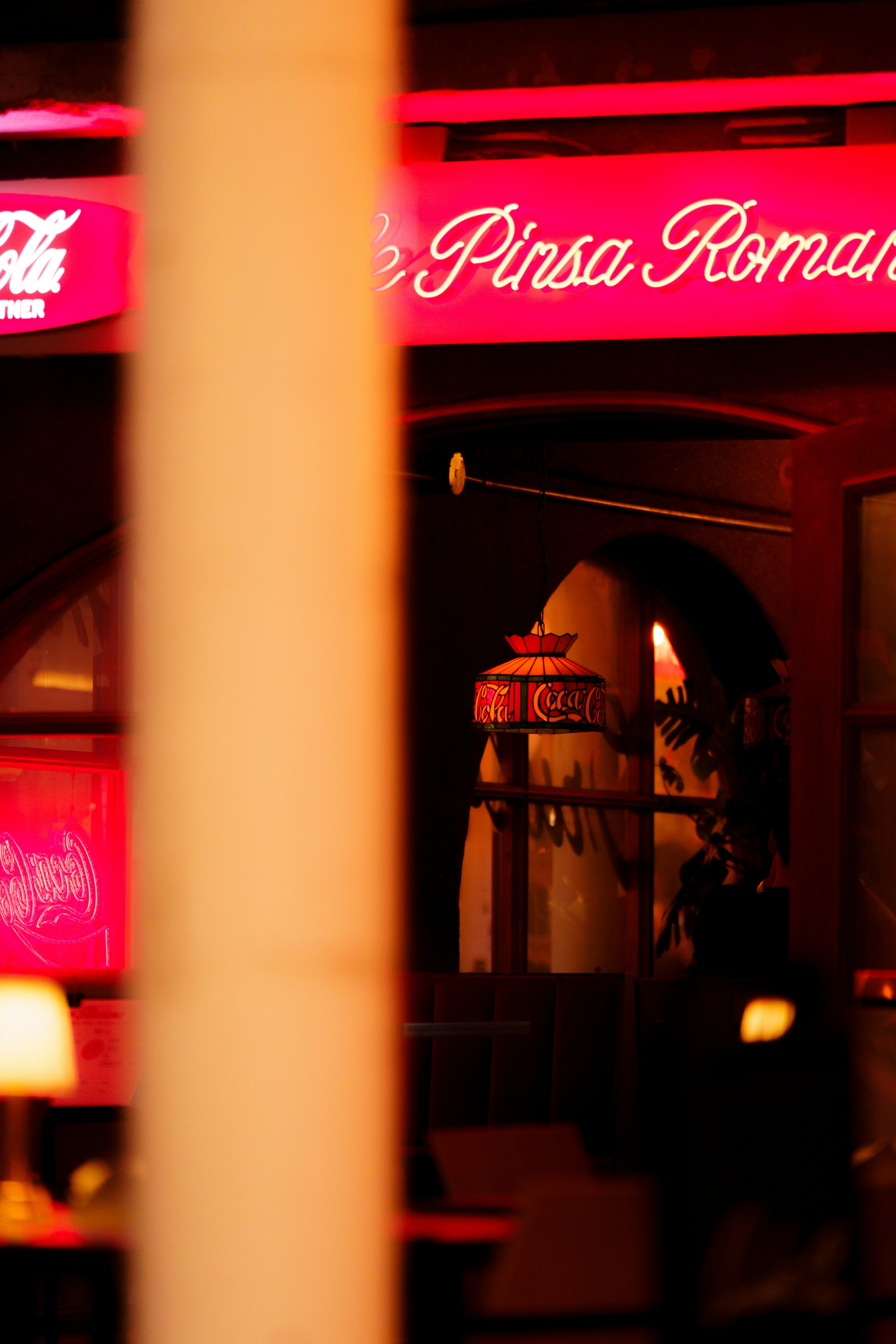 A stained glass lamp hanging in a restaurant with red neon signage