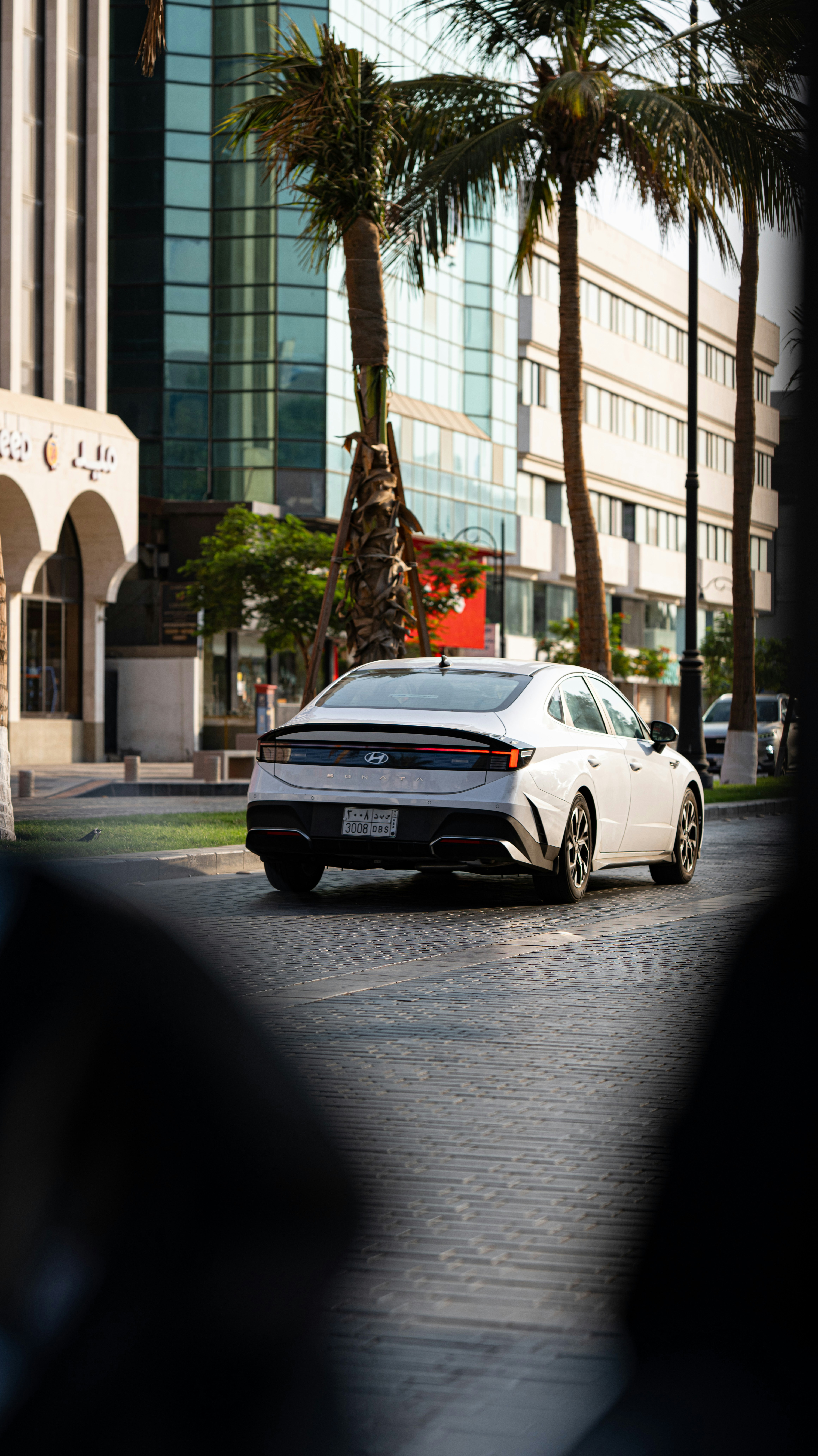 A white Hyundai Sonata driving on a paved city street with palm trees