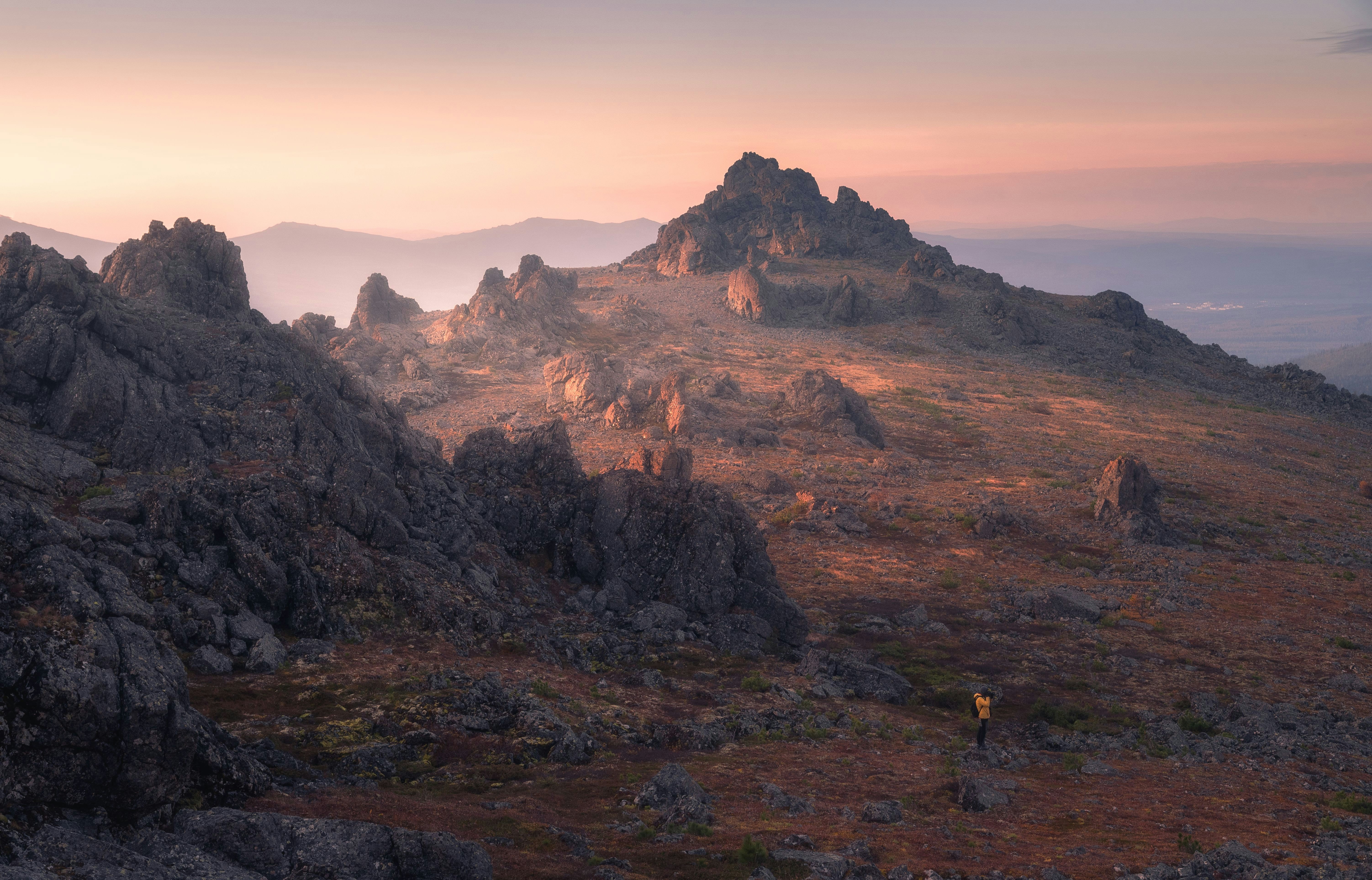 A person in a yellow jacket standing on a rocky mountain slope at golden hour