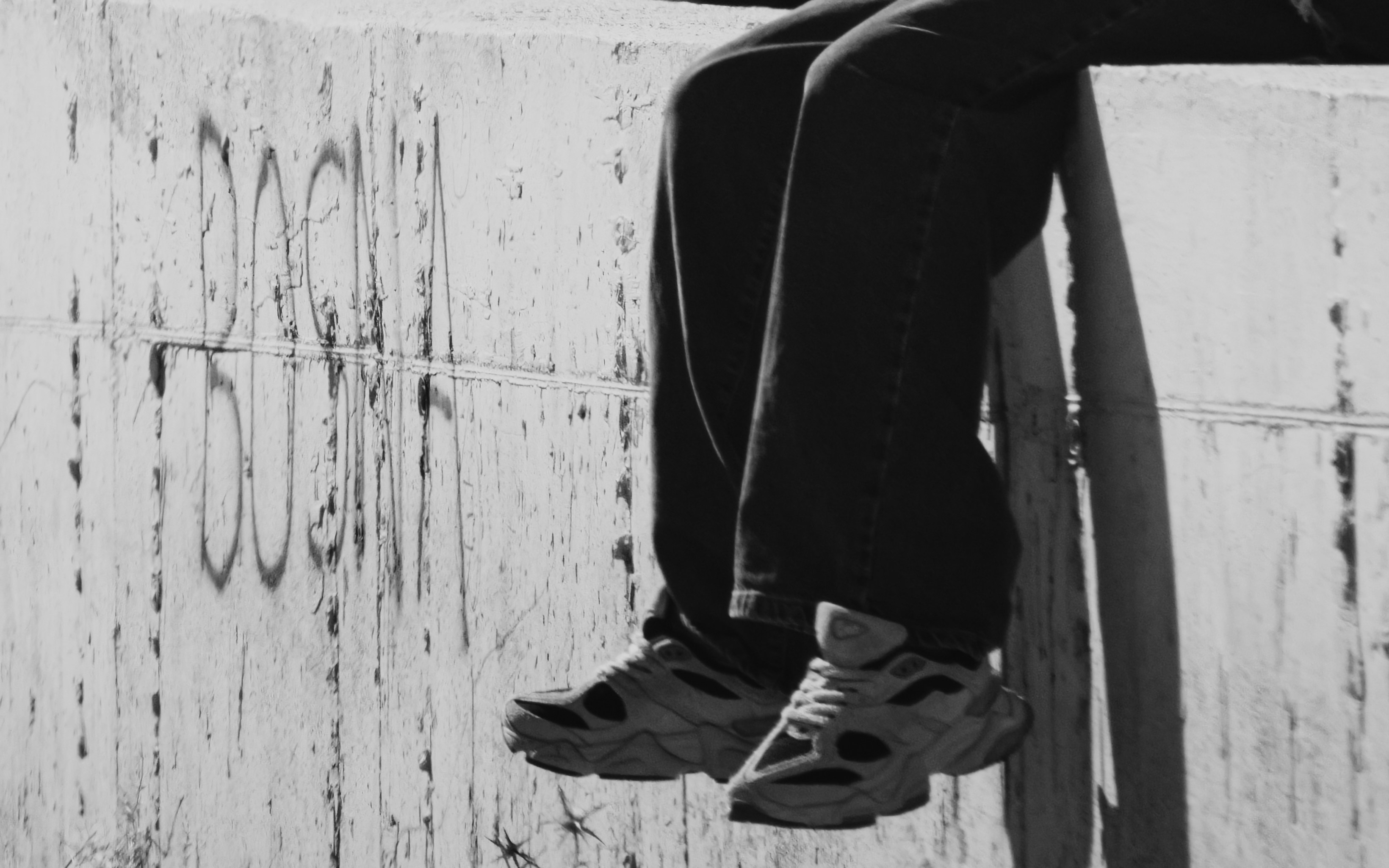 A person in jeans and sneakers perched on a concrete wall with graffiti
