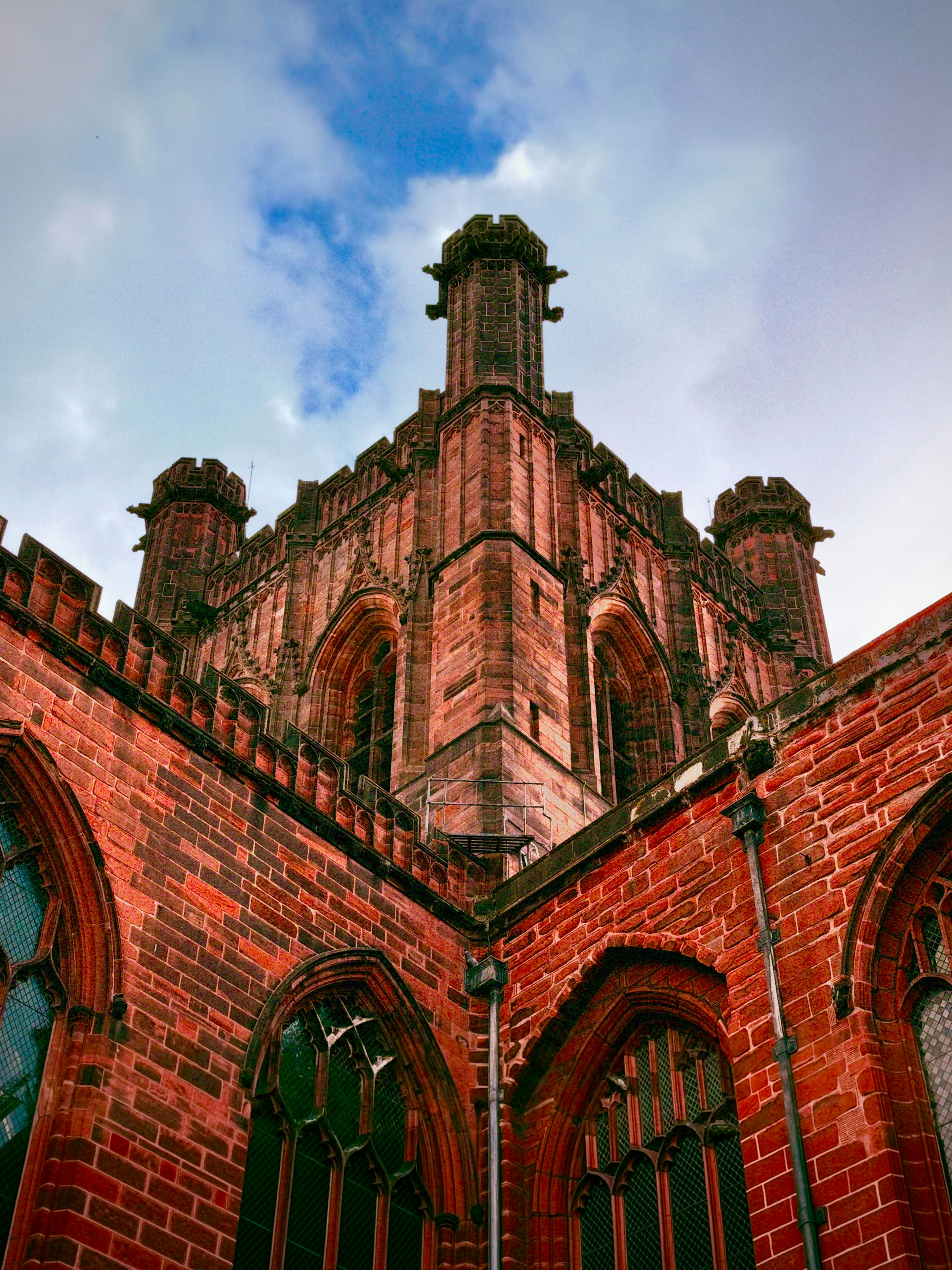 A red brick gothic cathedral tower with arched windows against a cloudy sky
