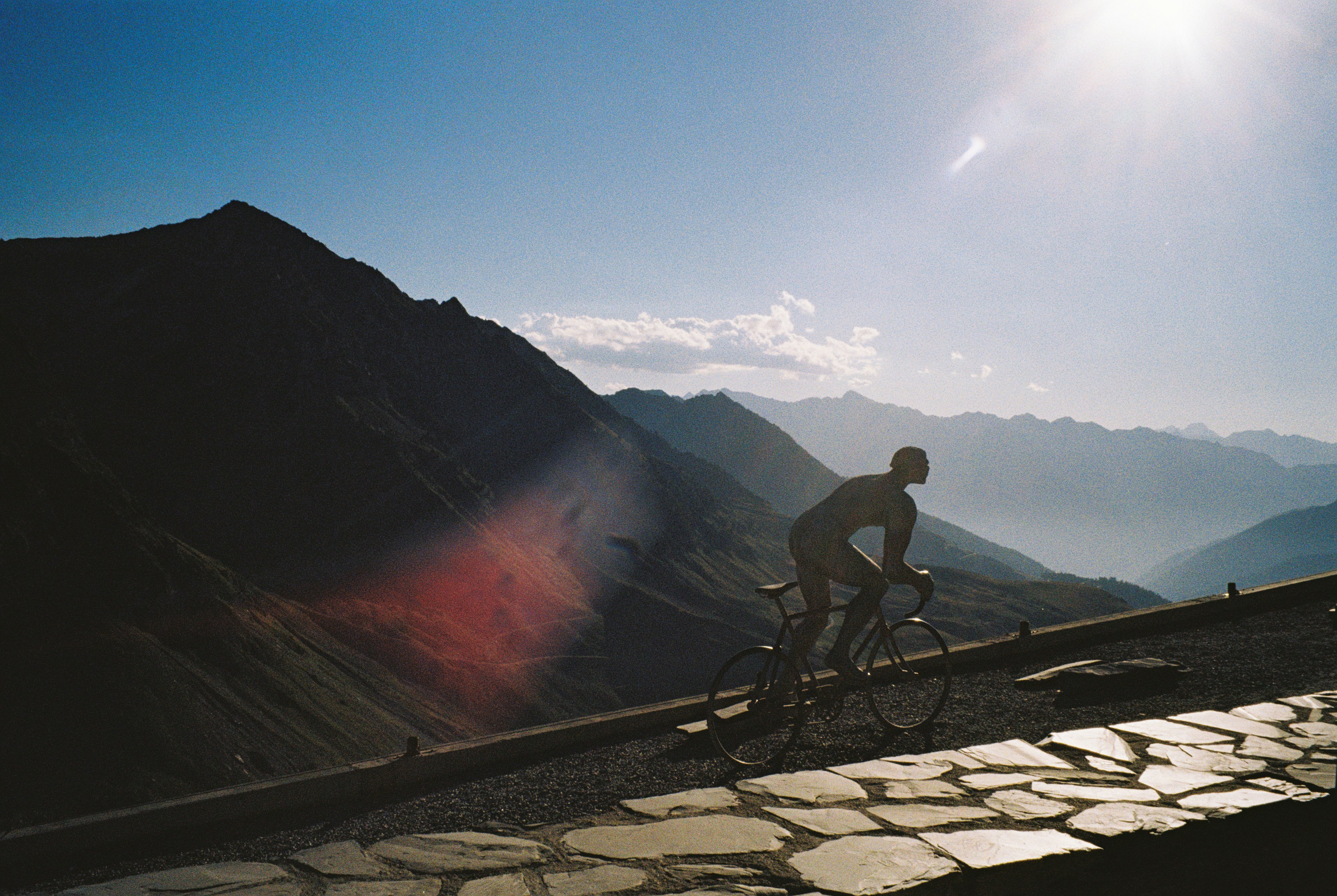 A cyclist in silhouette against a bright sky and rugged mountain peaks