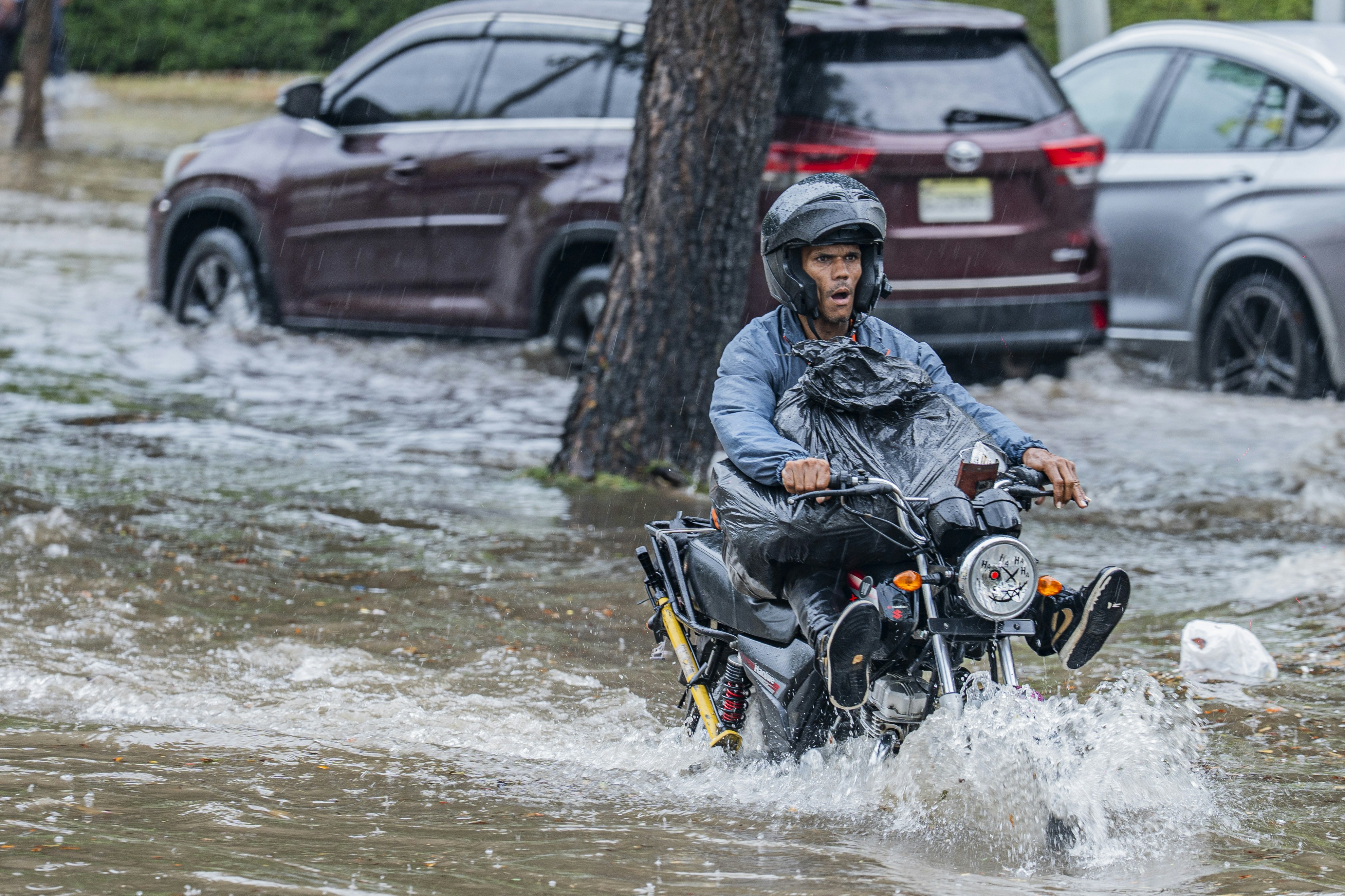 A person in a helmet riding a motorcycle through a flooded city street
