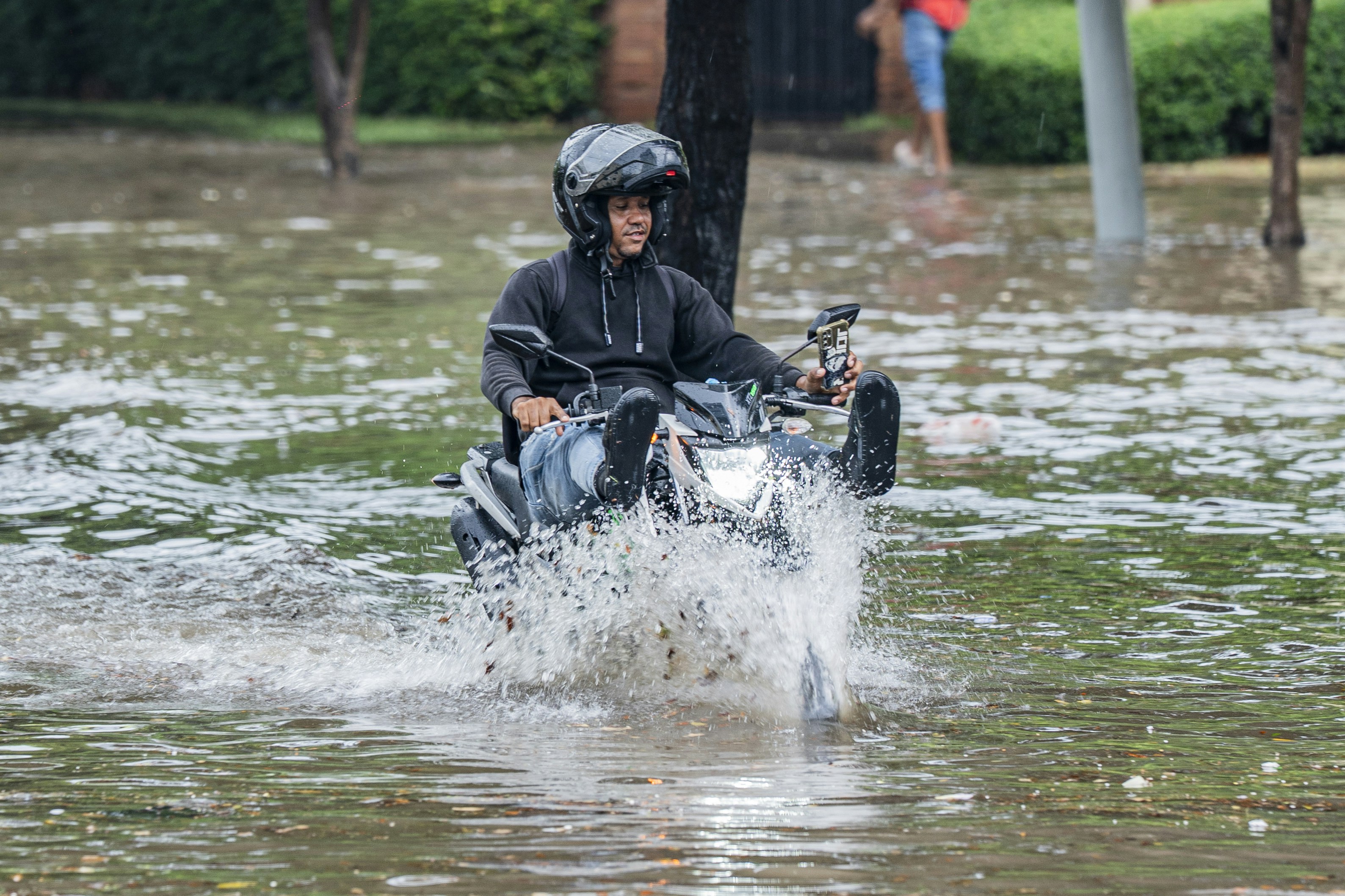 A person in a helmet riding a motorcycle through deep floodwater on a street