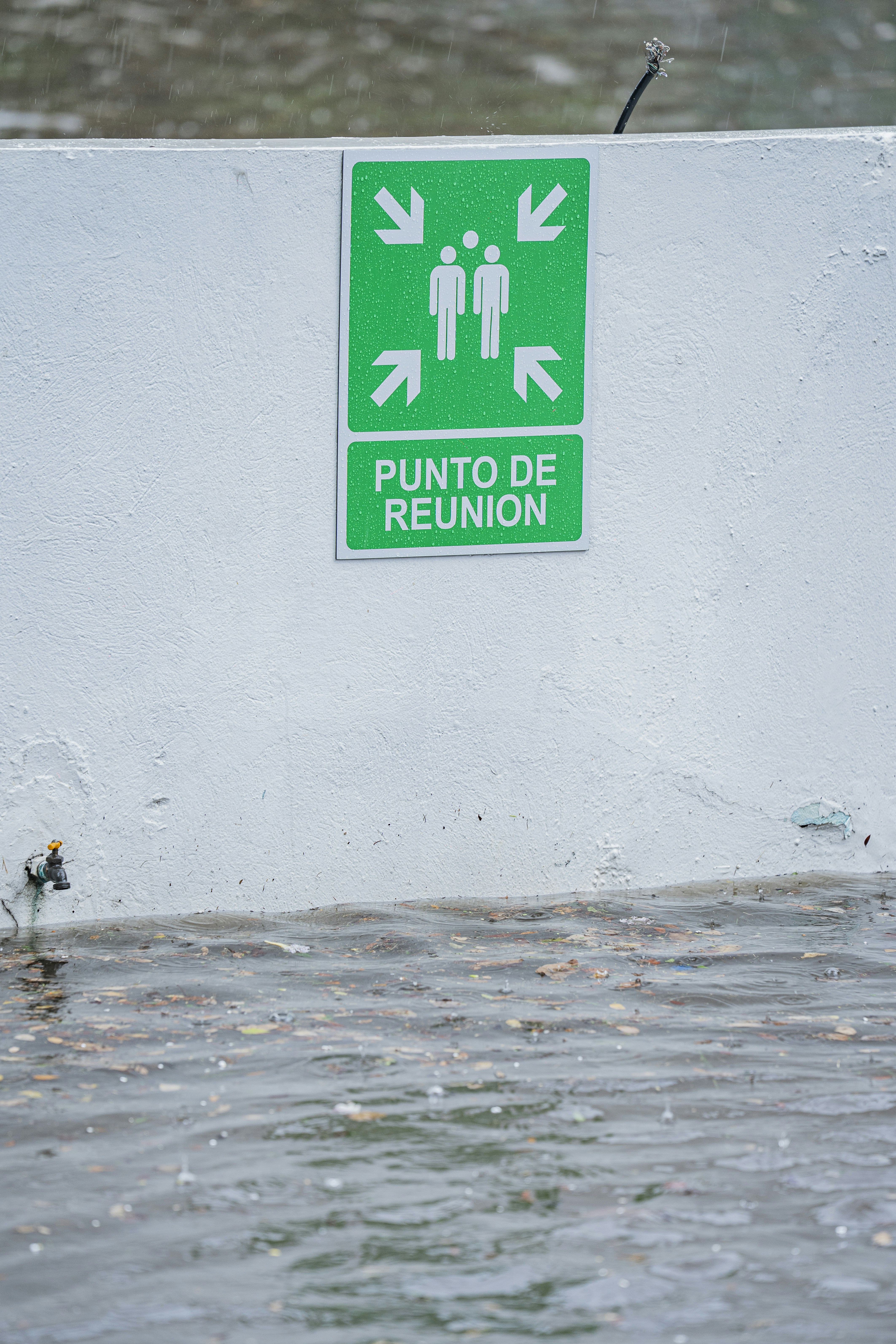 A green assembly point sign on a white wall above flooded water
