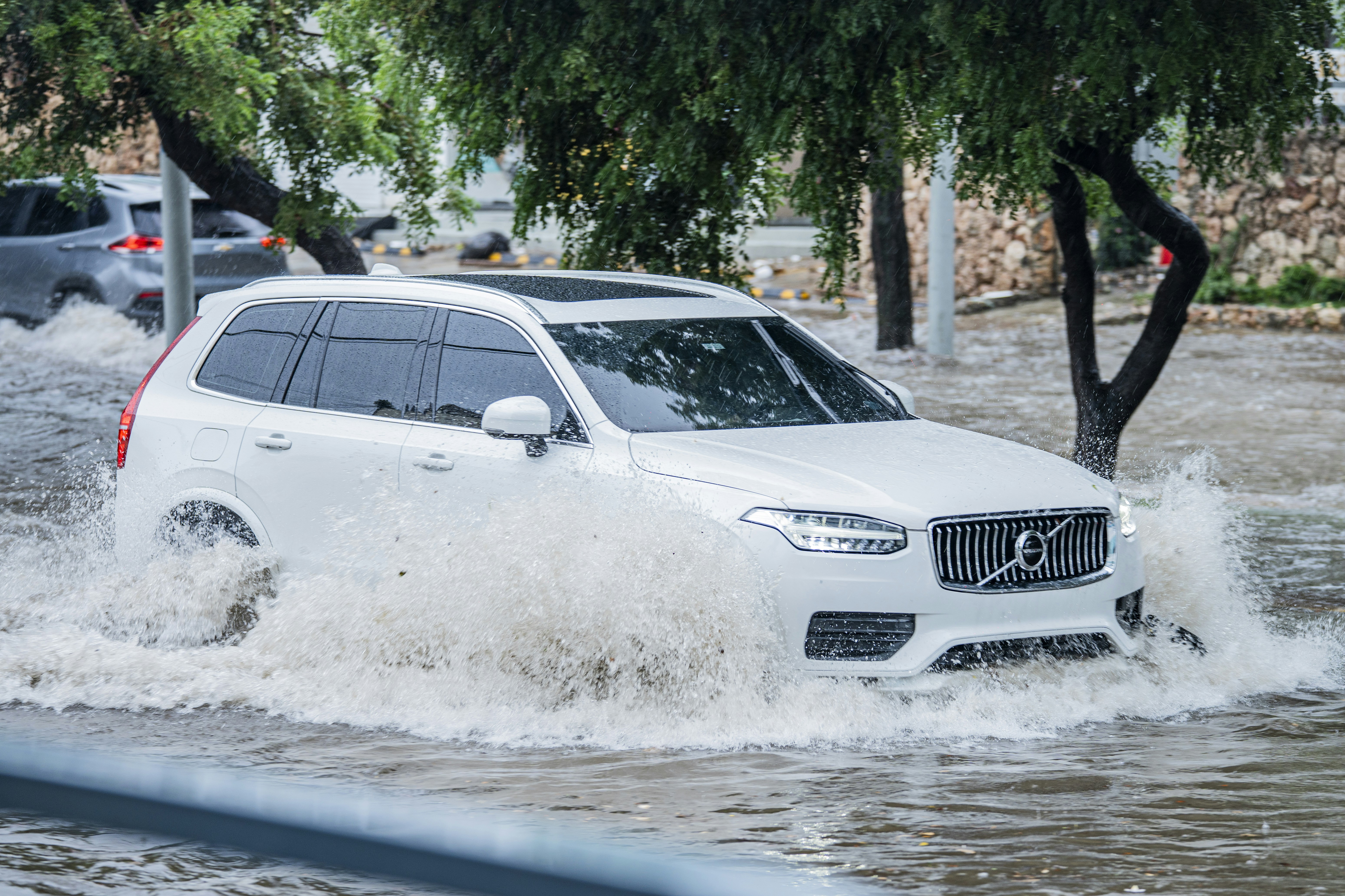 A white SUV driving through deep floodwater on a rain-slicked city street