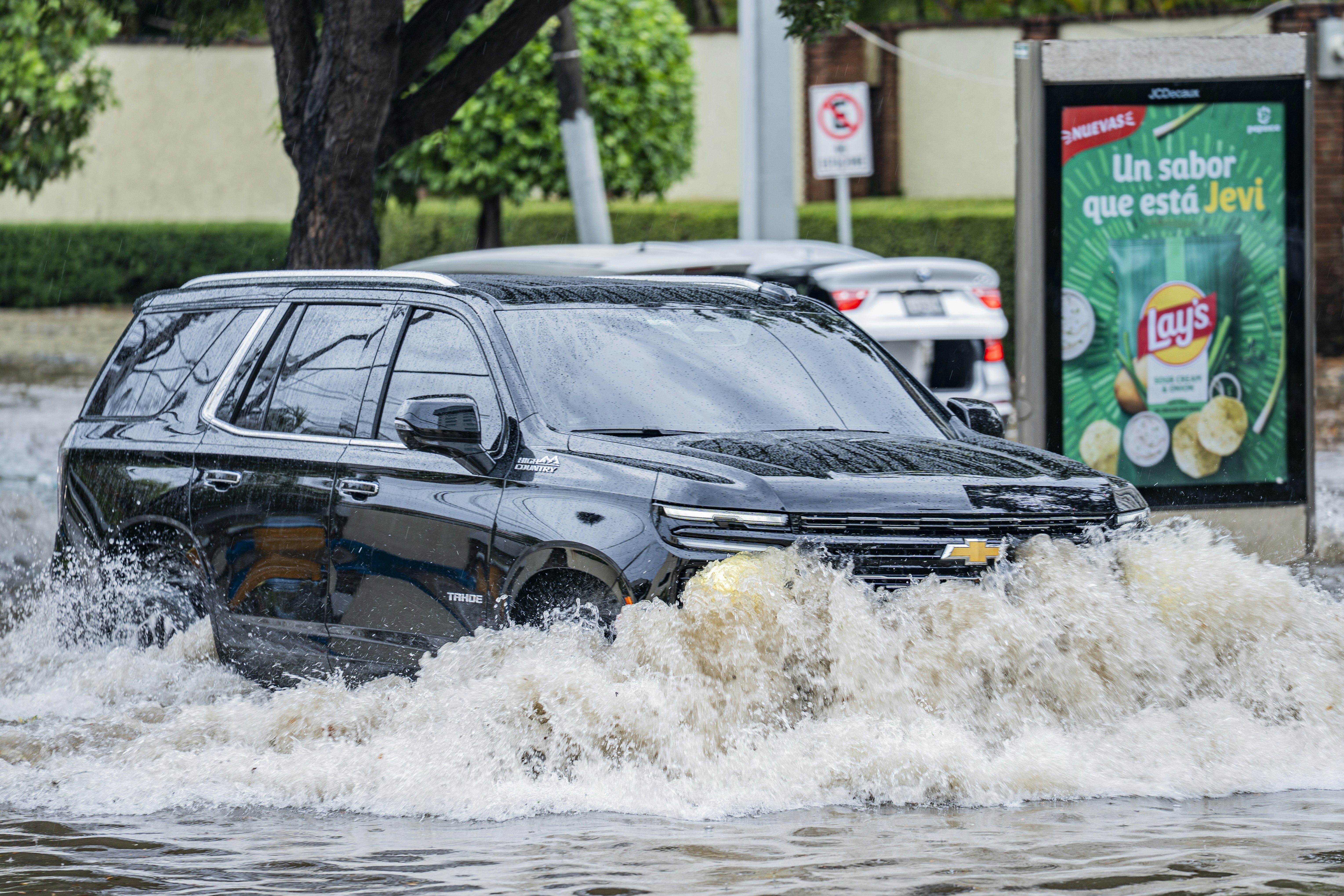 A black SUV driving through deep floodwater on a city street