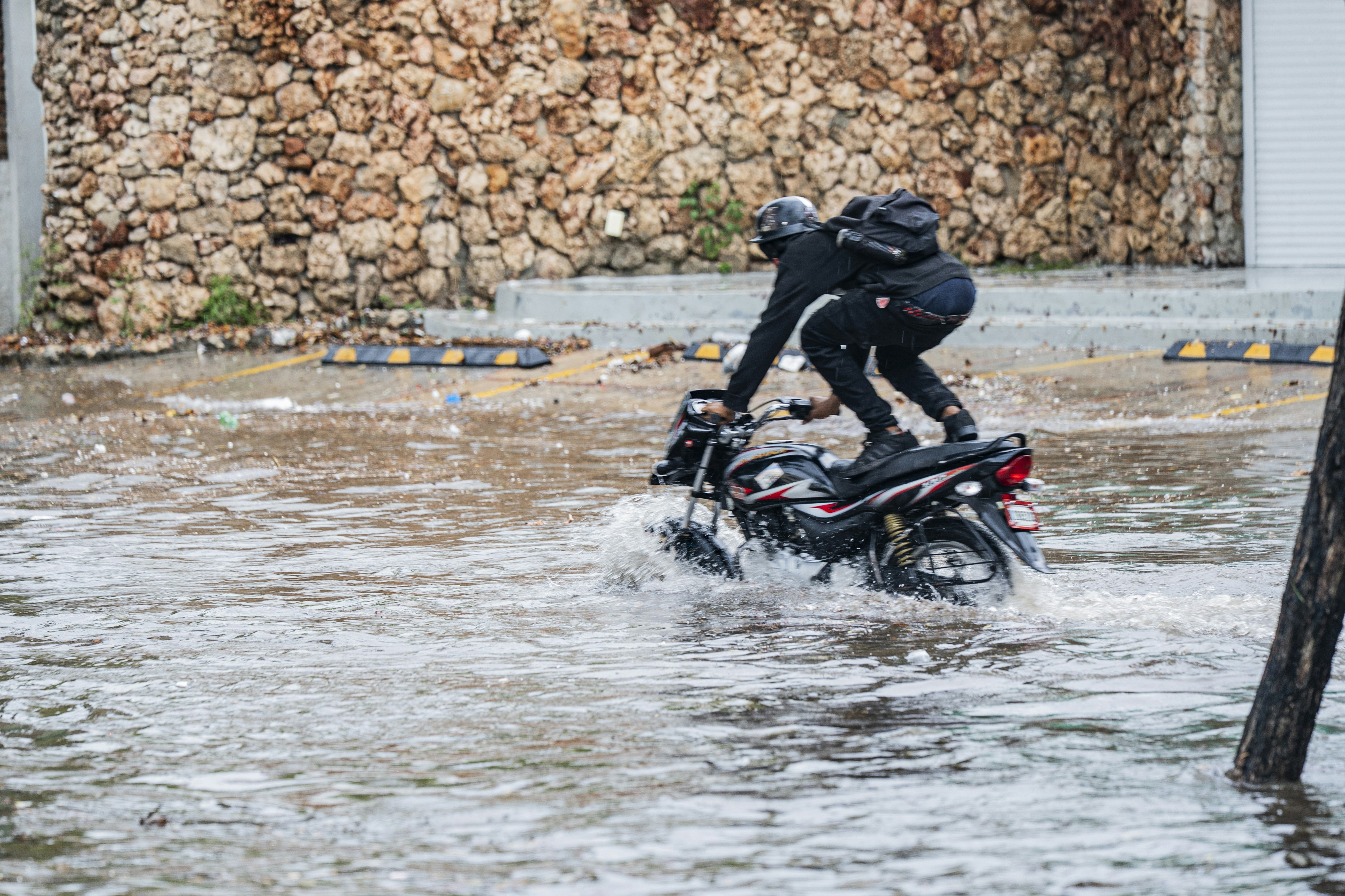 A person with a backpack riding a motorcycle through a flooded street
